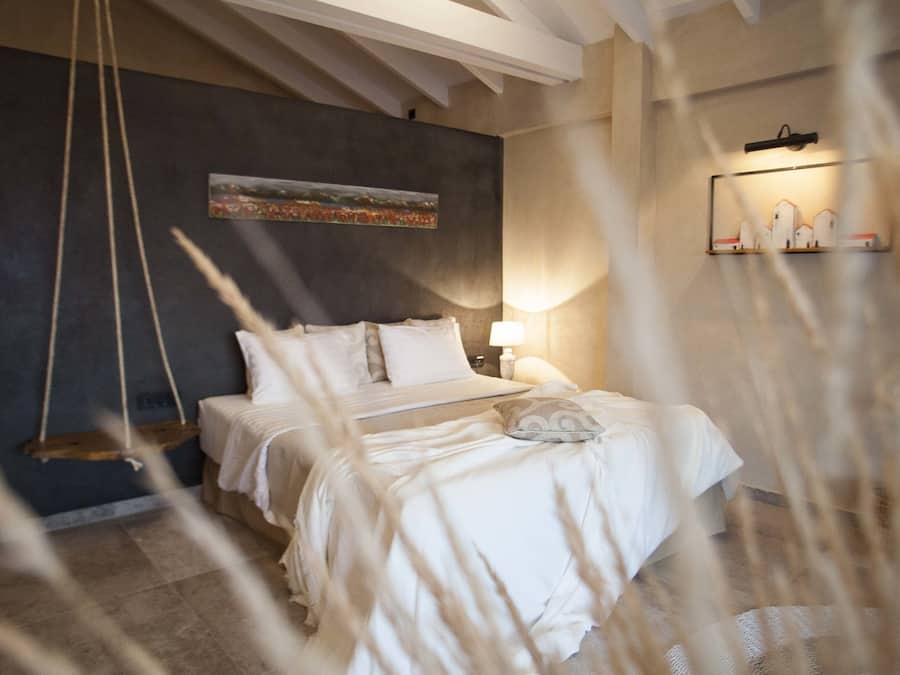 Un dormitorio con cama, una hamaca colgante, un cuadro en la pared y una estantería con objetos decorativos.