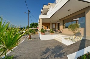 Una casa moderna de dos pisos con techo plano, balcón y patio con mobiliario exterior.