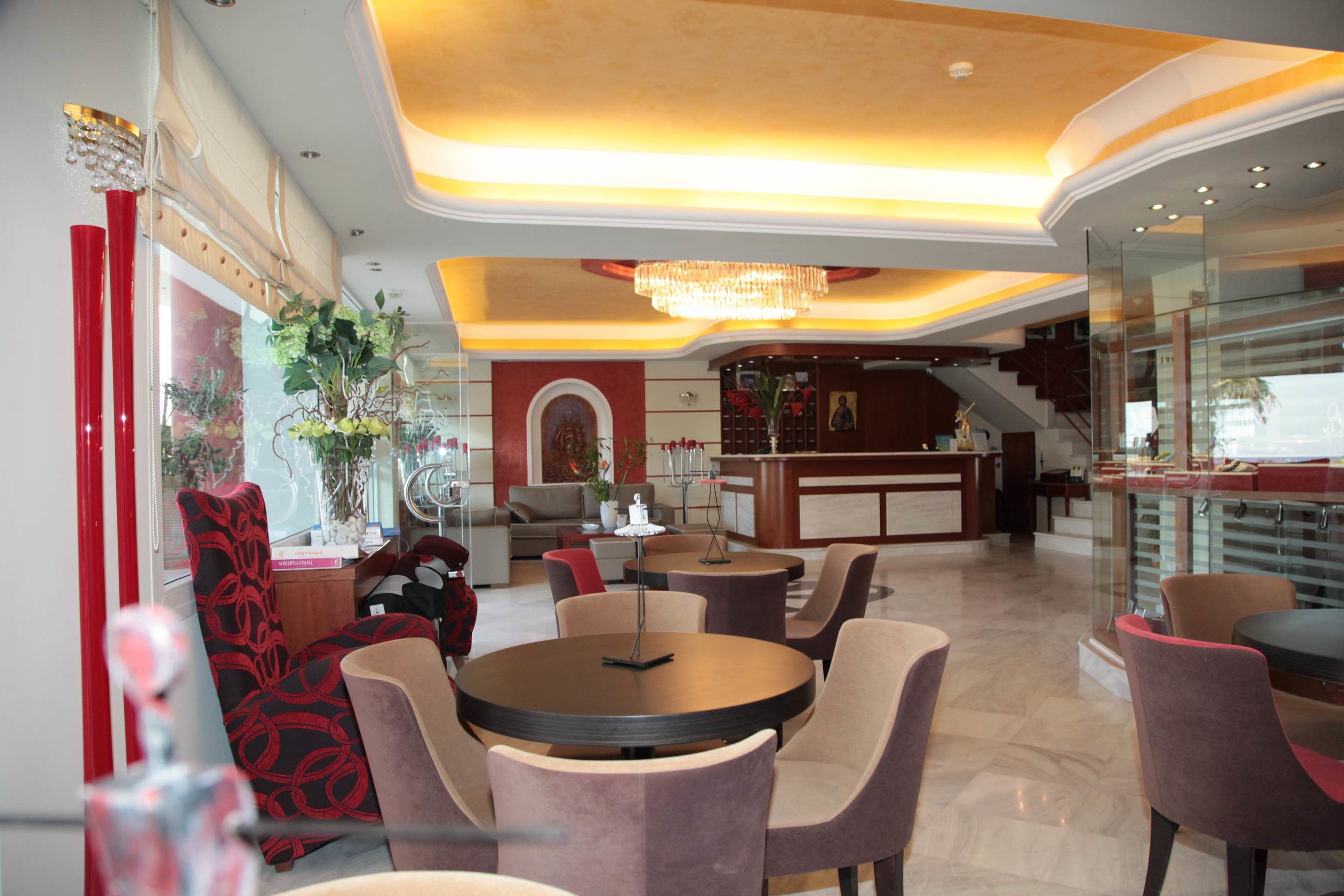 Un vestíbulo de hotel con mesas y sillas redondas, una recepción y una escalera que conduce a un nivel superior.