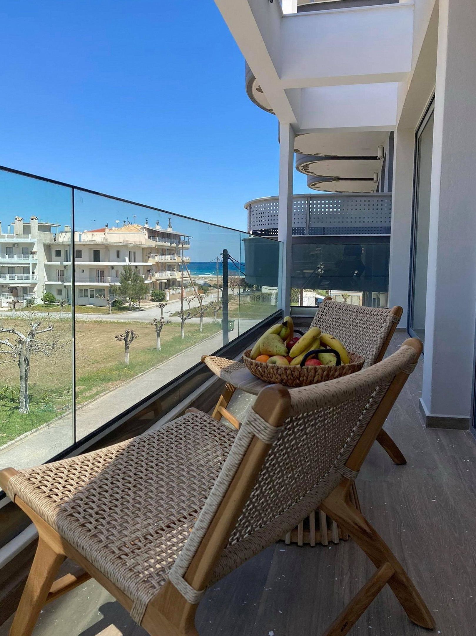 Un balcón con sillas de mimbre, una cesta de frutas y vistas a edificios y al mar.