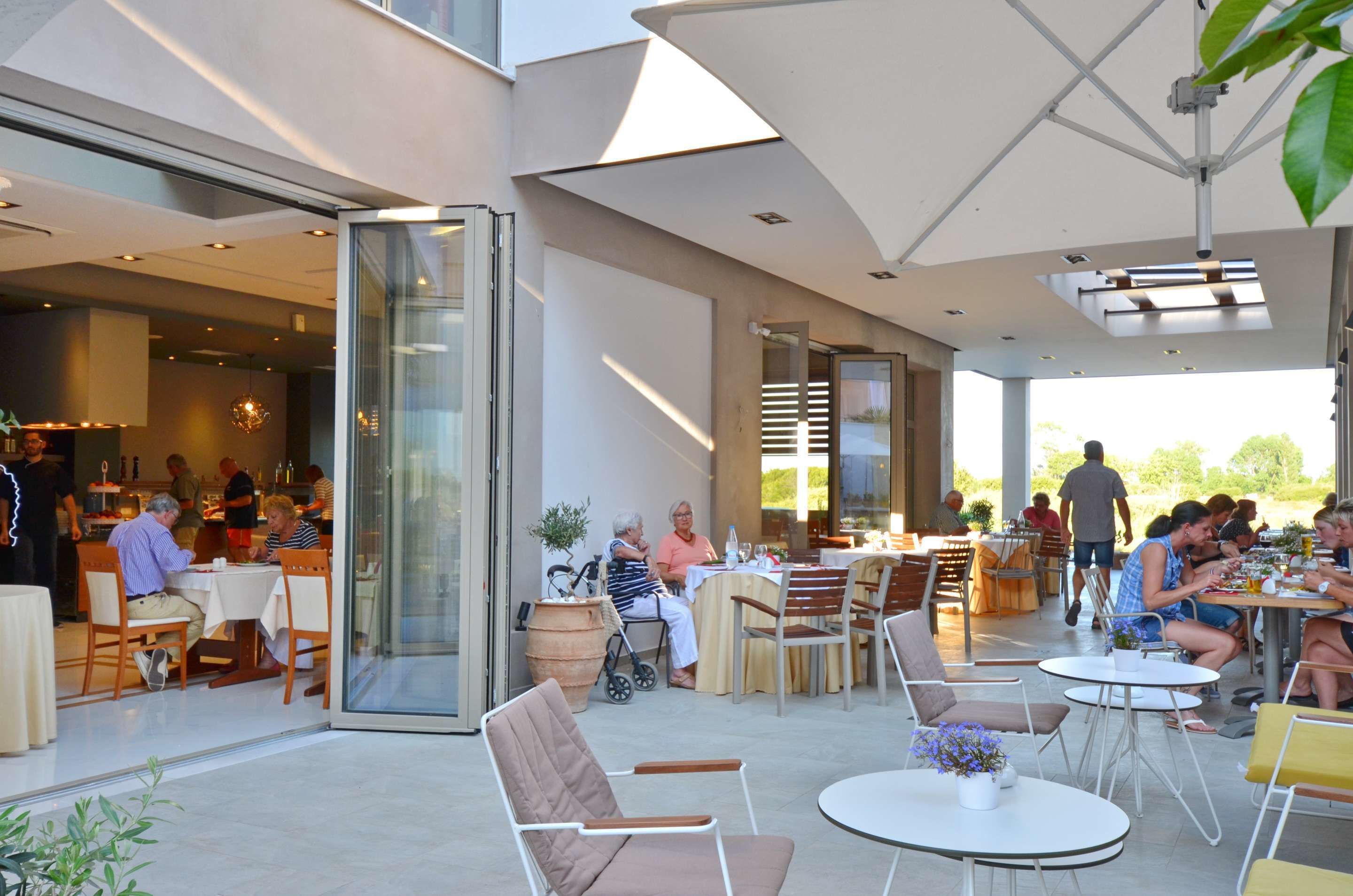 Un área de comedor al aire libre con mesas y sillas, una entrada con puerta de vidrio y vistas al exterior.