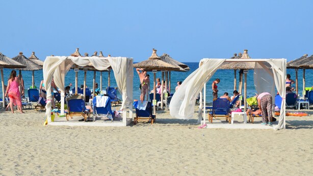 Una playa con sombrillas de paja y sillas de playa, algunas con cortinas blancas.