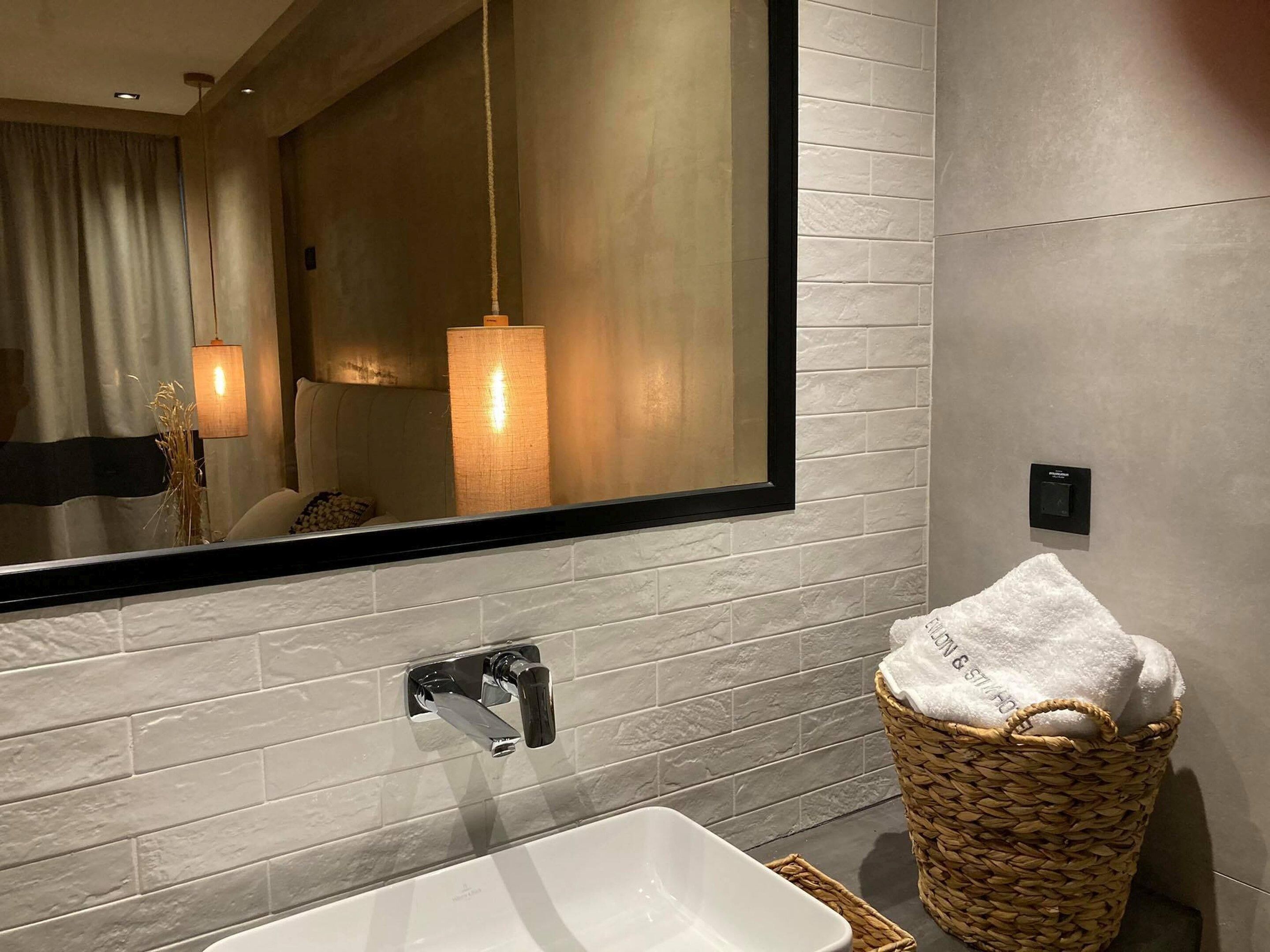 Une salle de bain moderne avec un grand miroir, un lavabo blanc et un panier en osier contenant une serviette.