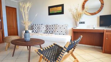 A modern living room with a sofa, a round wooden table, a woven chair, a TV, and a decorative mirror.