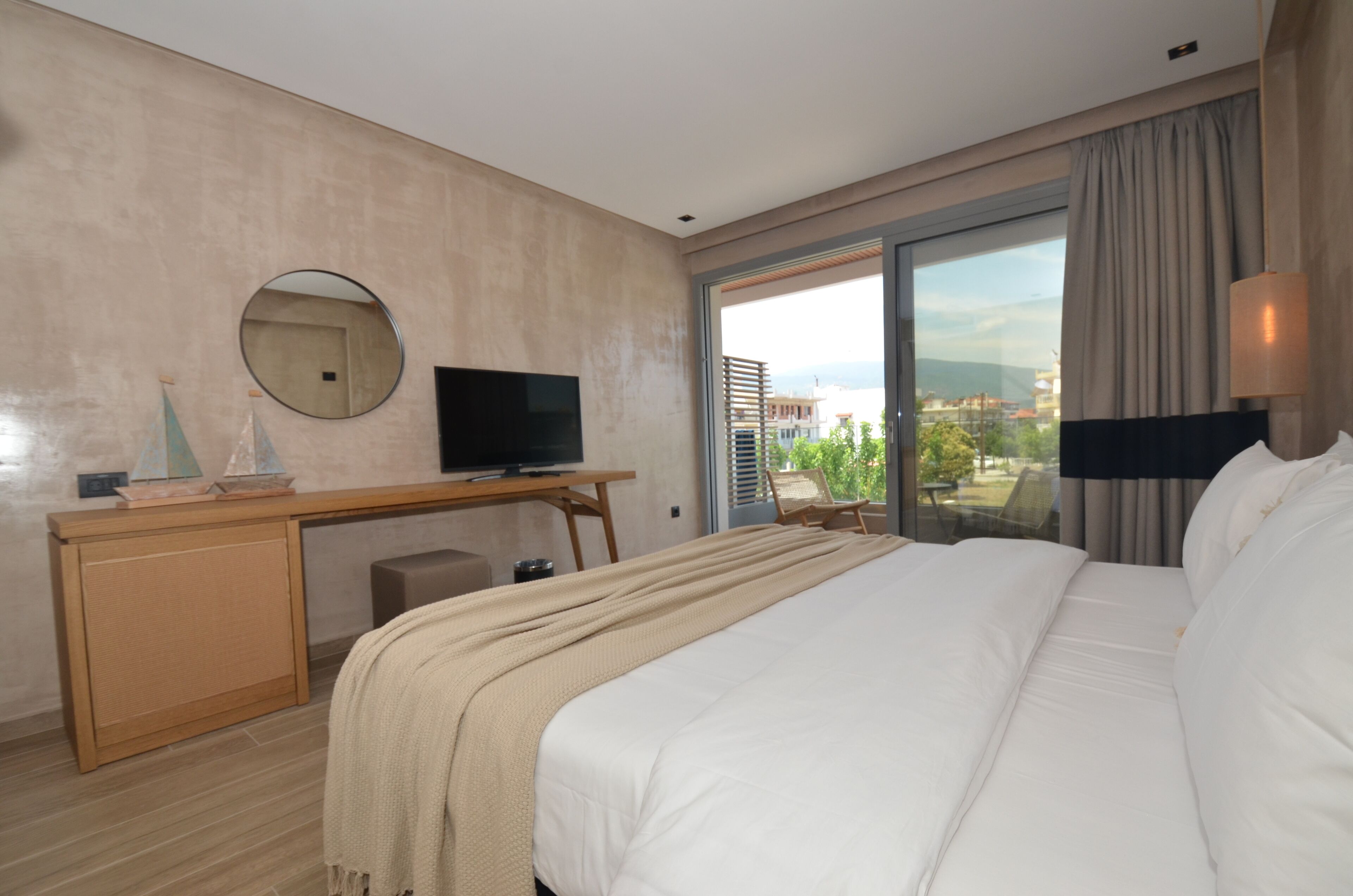 A hotel room with a bed, a desk with a television, a chair, and a large window offering a city view.