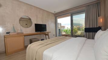A hotel room with a bed, a desk with a television, a chair, and a large window offering a city view.