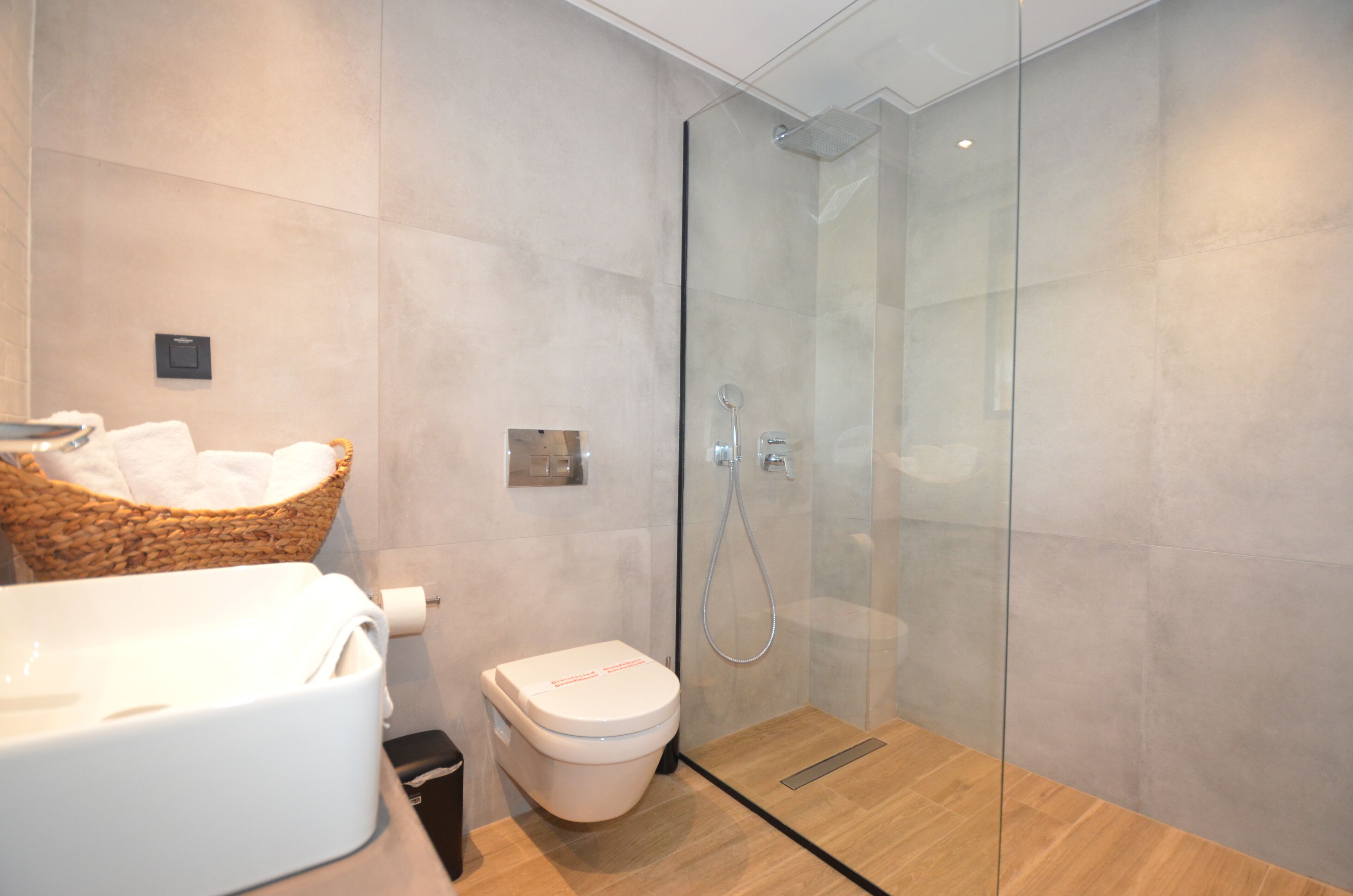 A modern bathroom with a glass-enclosed shower, a white toilet, and a wicker basket with towels.