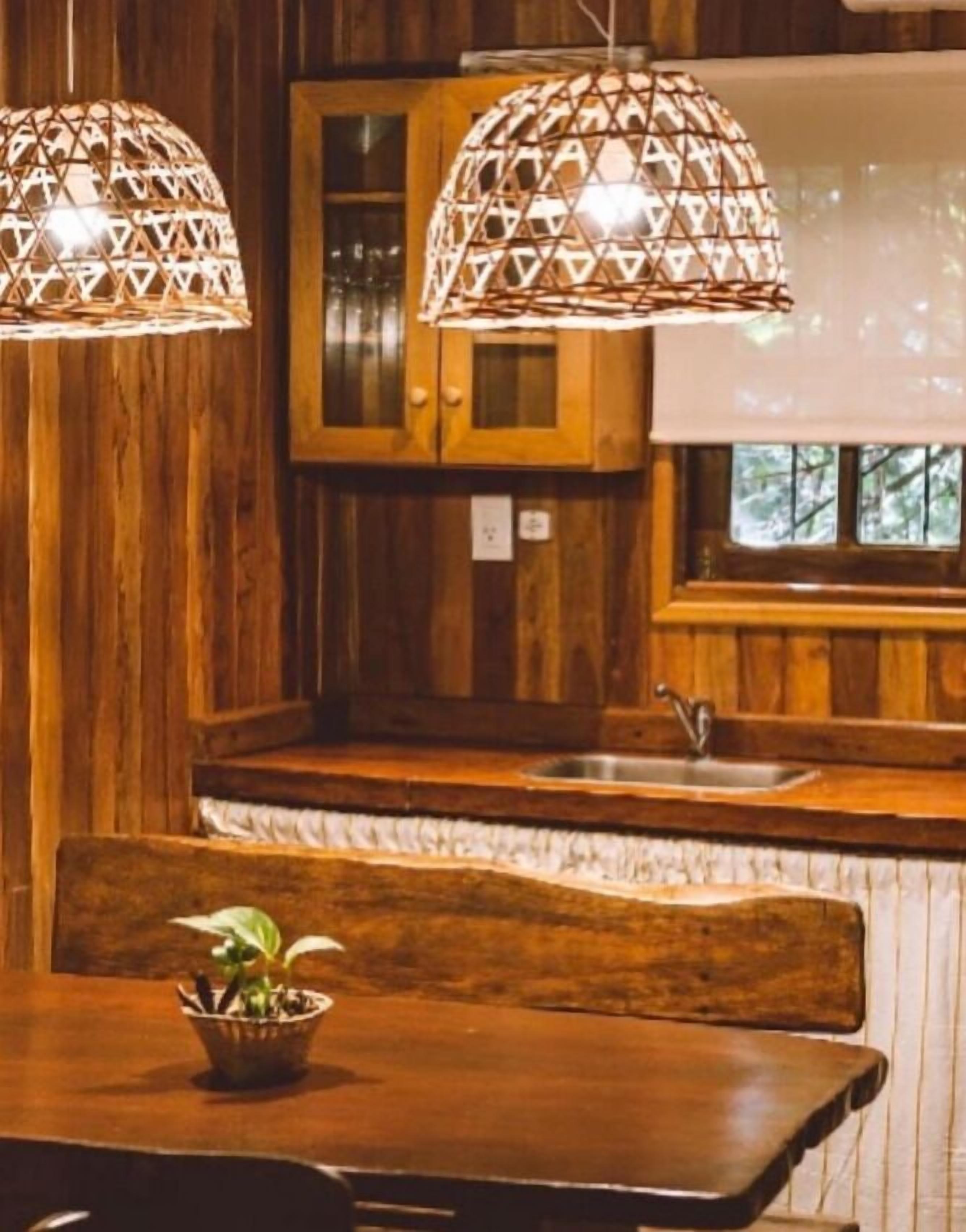 Cucina in legno con due lampade a sospensione, una panca in legno e una finestra vista alberi.