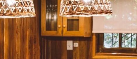 Una cocina de madera con dos lámparas colgantes, un banco de madera y una ventana con vistas a árboles.
