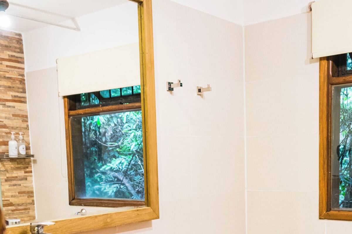 Un baño con tocador de madera, un espejo grande, un lavabo, una bañera y una ventana con vista a árboles.