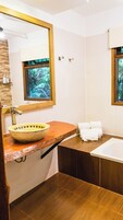 Un baño con tocador de madera, un espejo grande, un lavabo, una bañera y una ventana con vista a árboles.