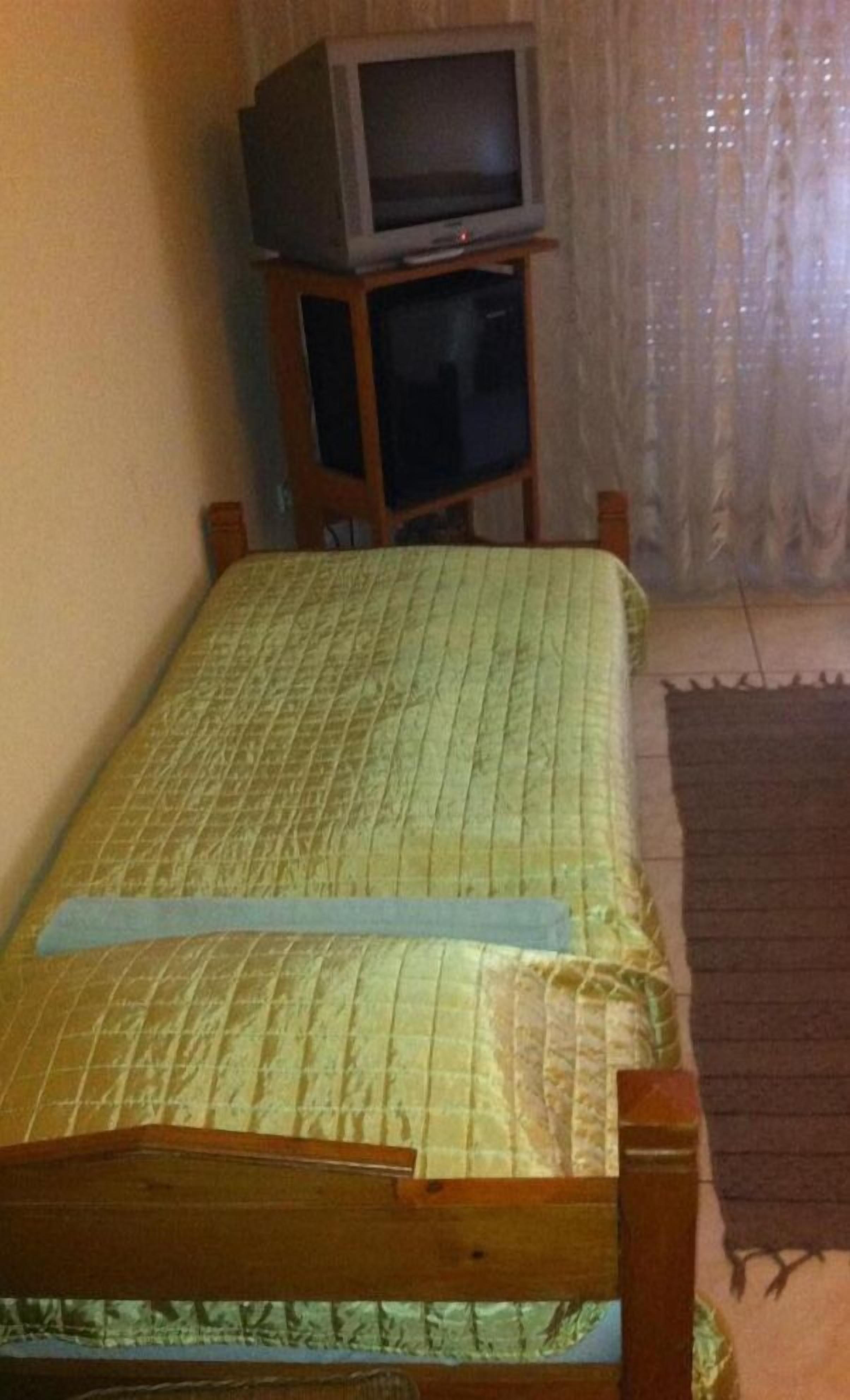 A small room with a single bed, a television on a wooden stand, and a curtain.