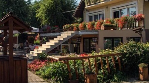 En toetagers bygning med balkon, træpergola og en belagt terrasse med plantekrukker.