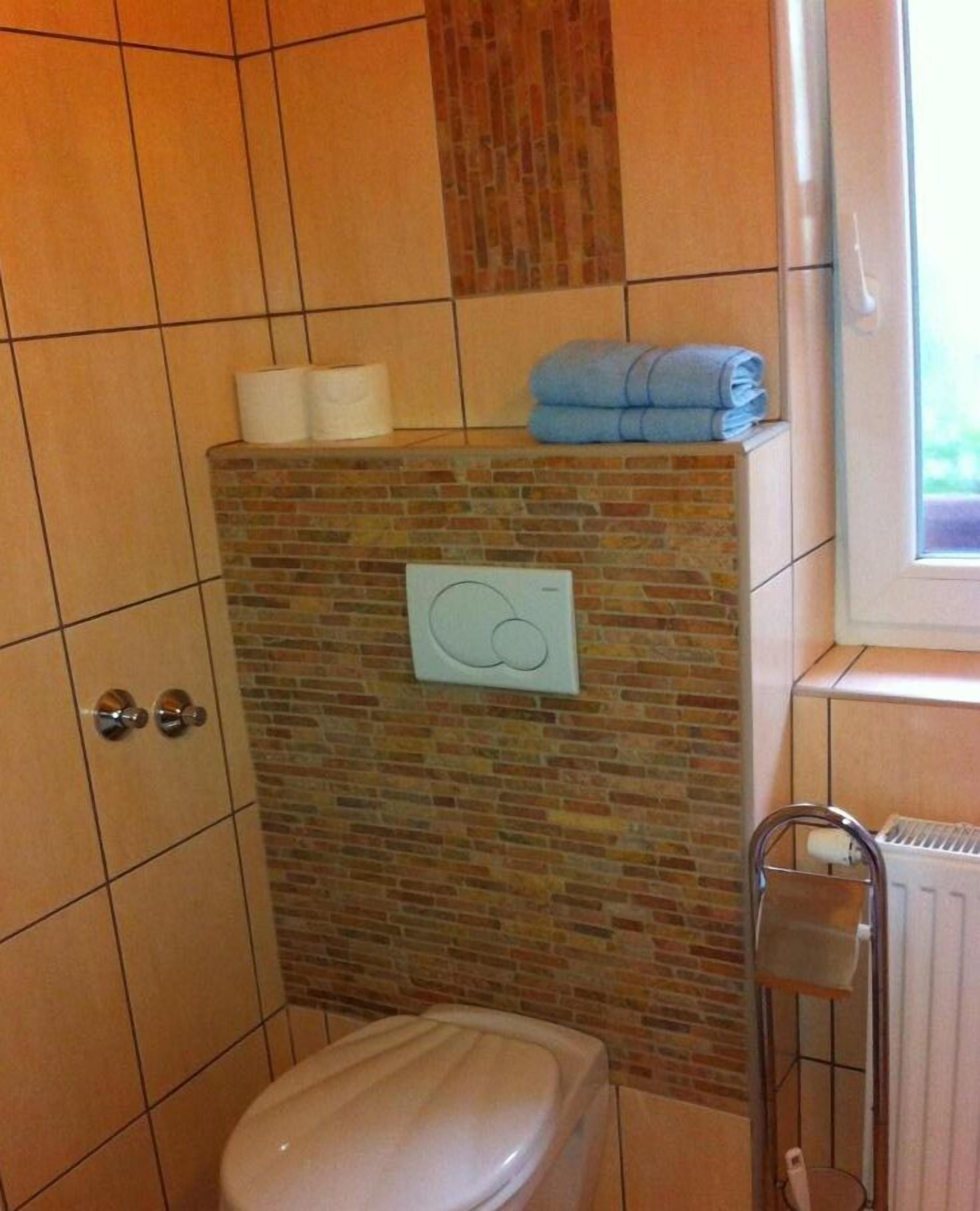 A bathroom with a toilet, a shower area with a tiled wall, and a radiator.