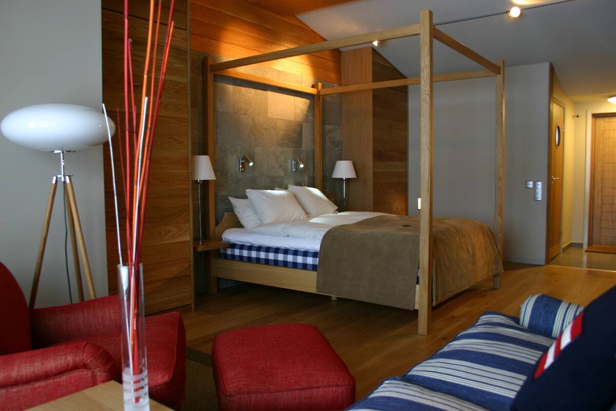 Een moderne slaapkamer met een hemelbed, houten vloeren en een rode gestoffeerde bank.