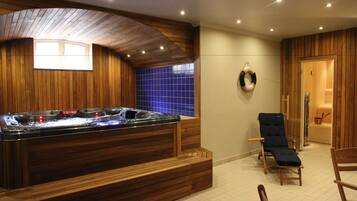 Zona de spa con hidromasaje, bancos de madera, una tumbona y pared de azulejos azules.