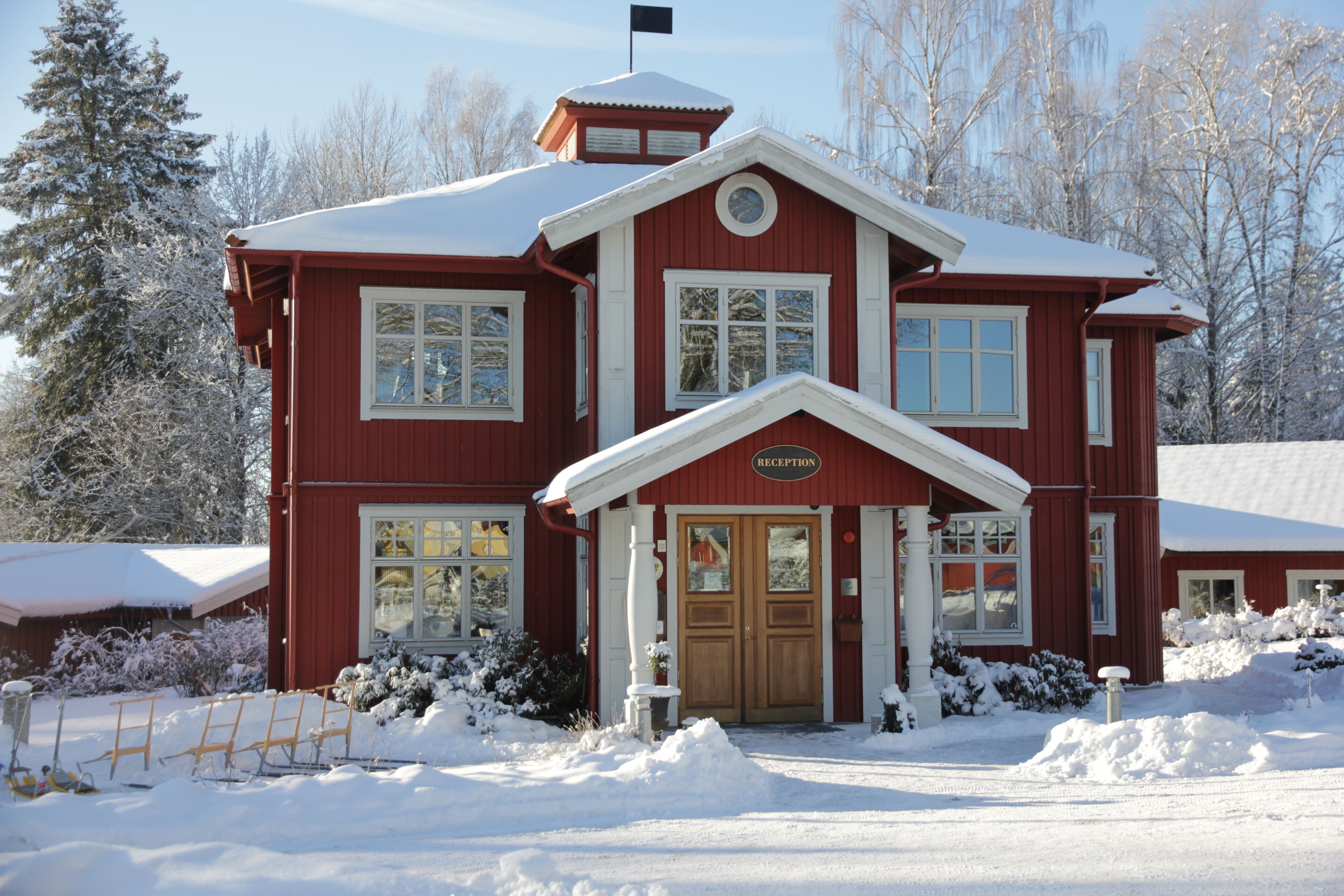 En röd byggnad med en skylt vid ingången där det står ”RECEPTION”, omgiven av snö.