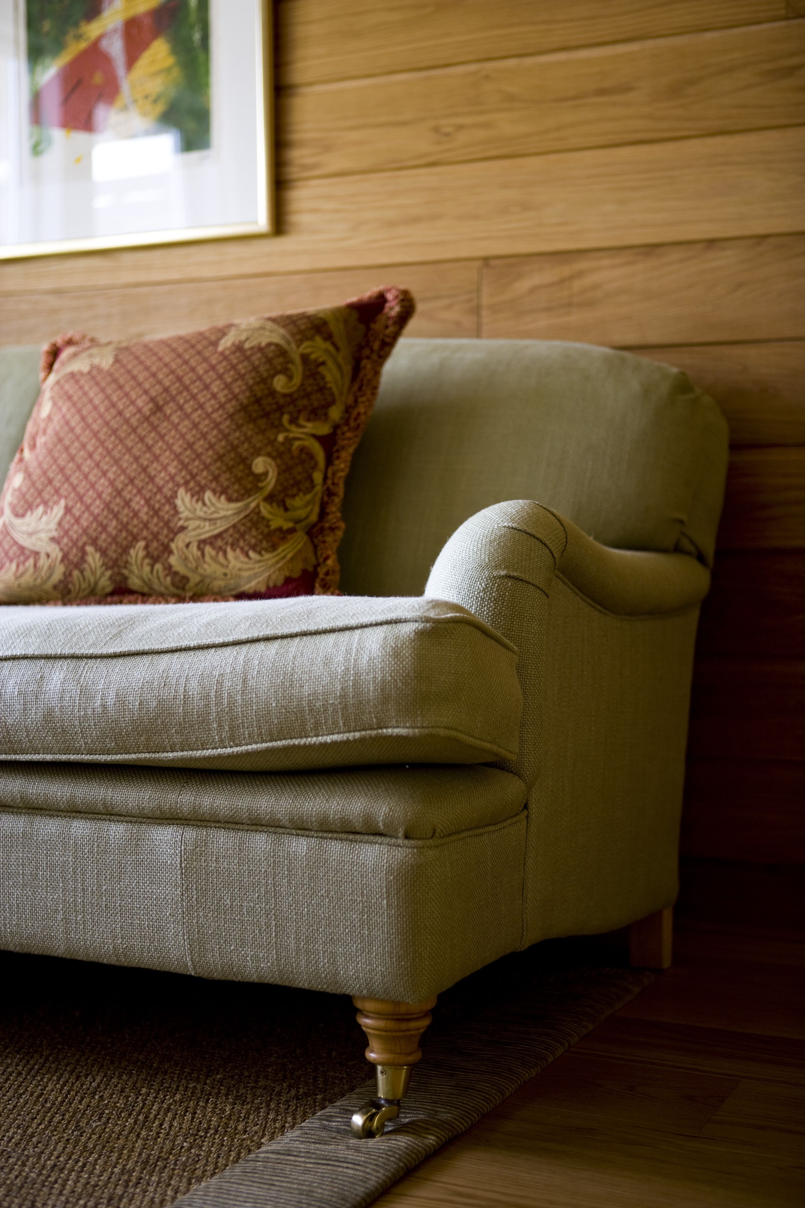 A sofa with a patterned cushion and wooden legs, positioned on a carpeted floor with a wooden wall in the background.