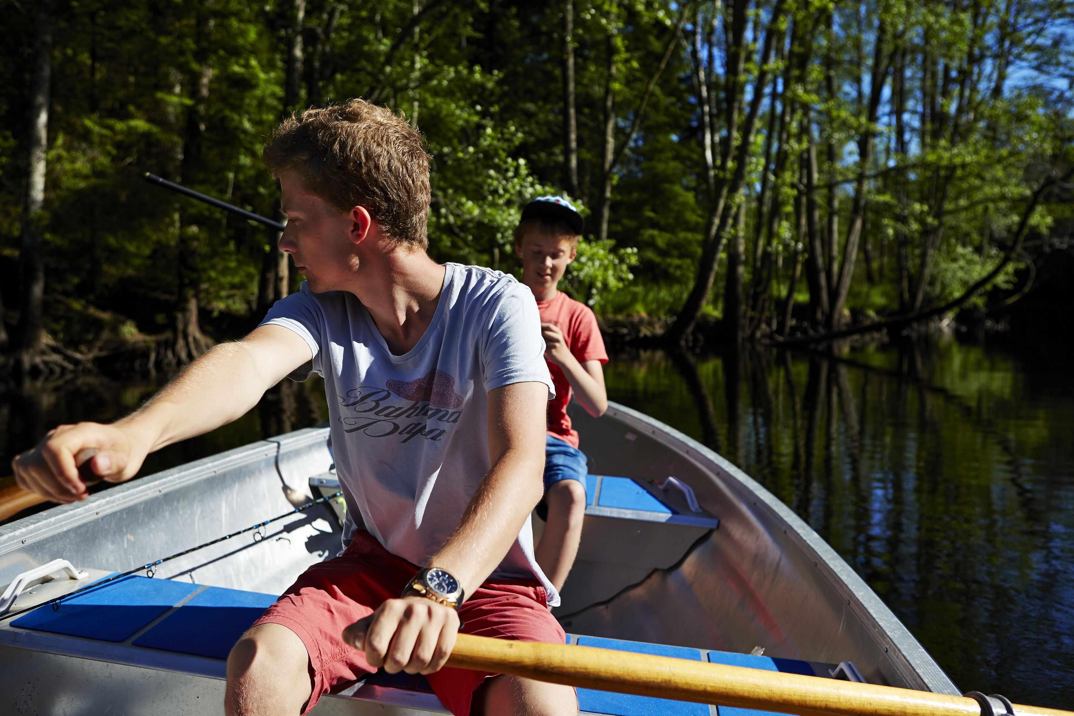 A person rowing a boat on a calm river surrounded by trees.