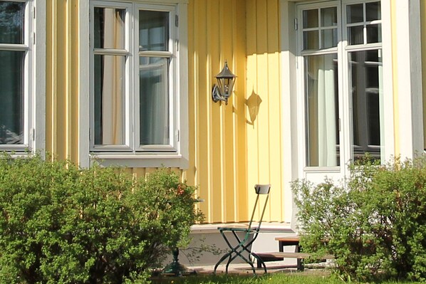 A yellow house with white trim, a bench, and a lamp on the porch. - HESTRAVIKEN HOTEL & SPA (Hestra)