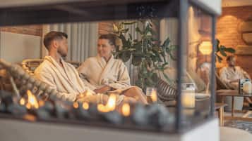 A couple in a cozy, well-lit room with a fireplace, comfortable seating, and a plant.