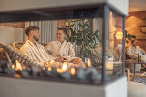 Una pareja en una habitación acogedora y bien iluminada, con chimenea, asientos cómodos y una planta.
