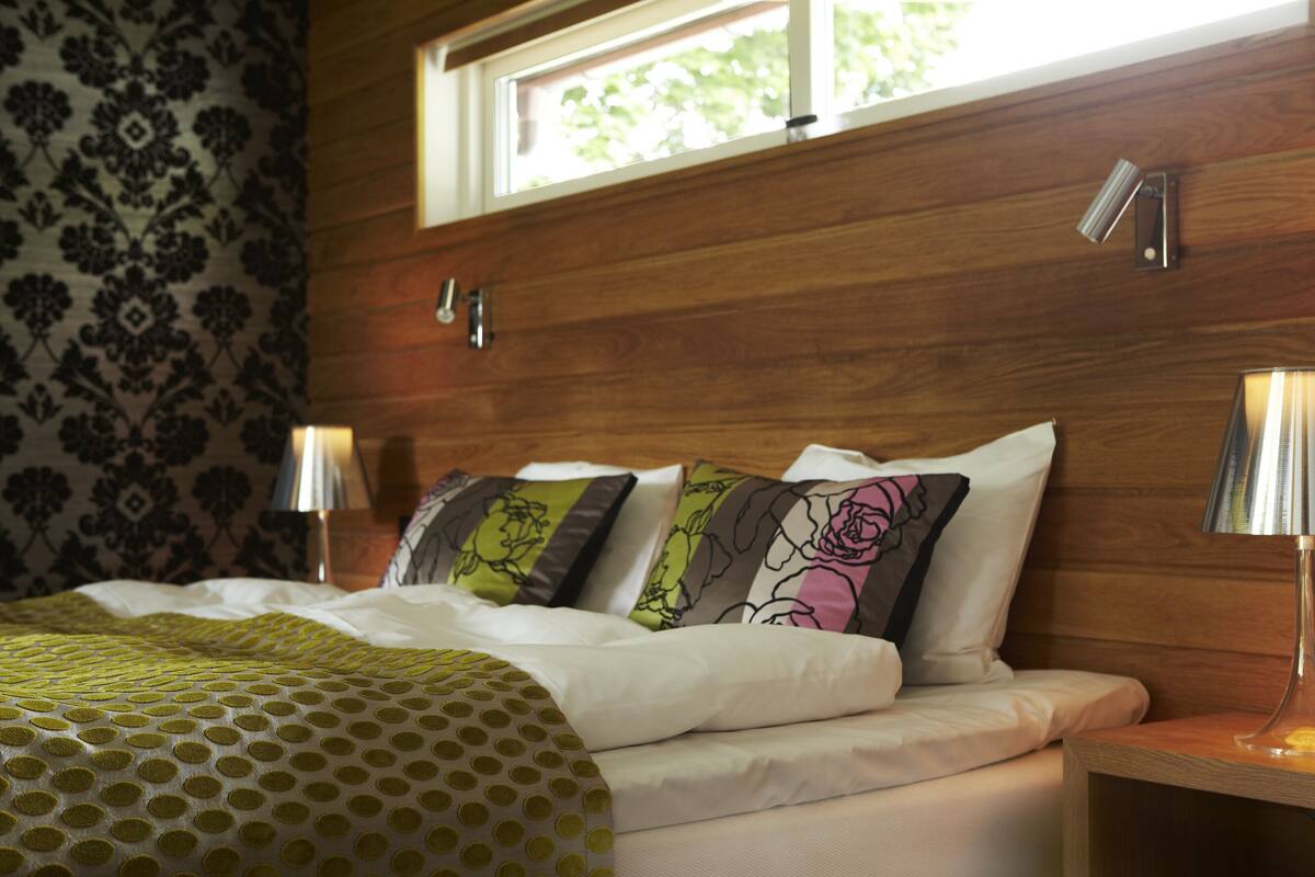 Een slaapkamer met een houten hoofdbord, een raam en twee bedlampjes.