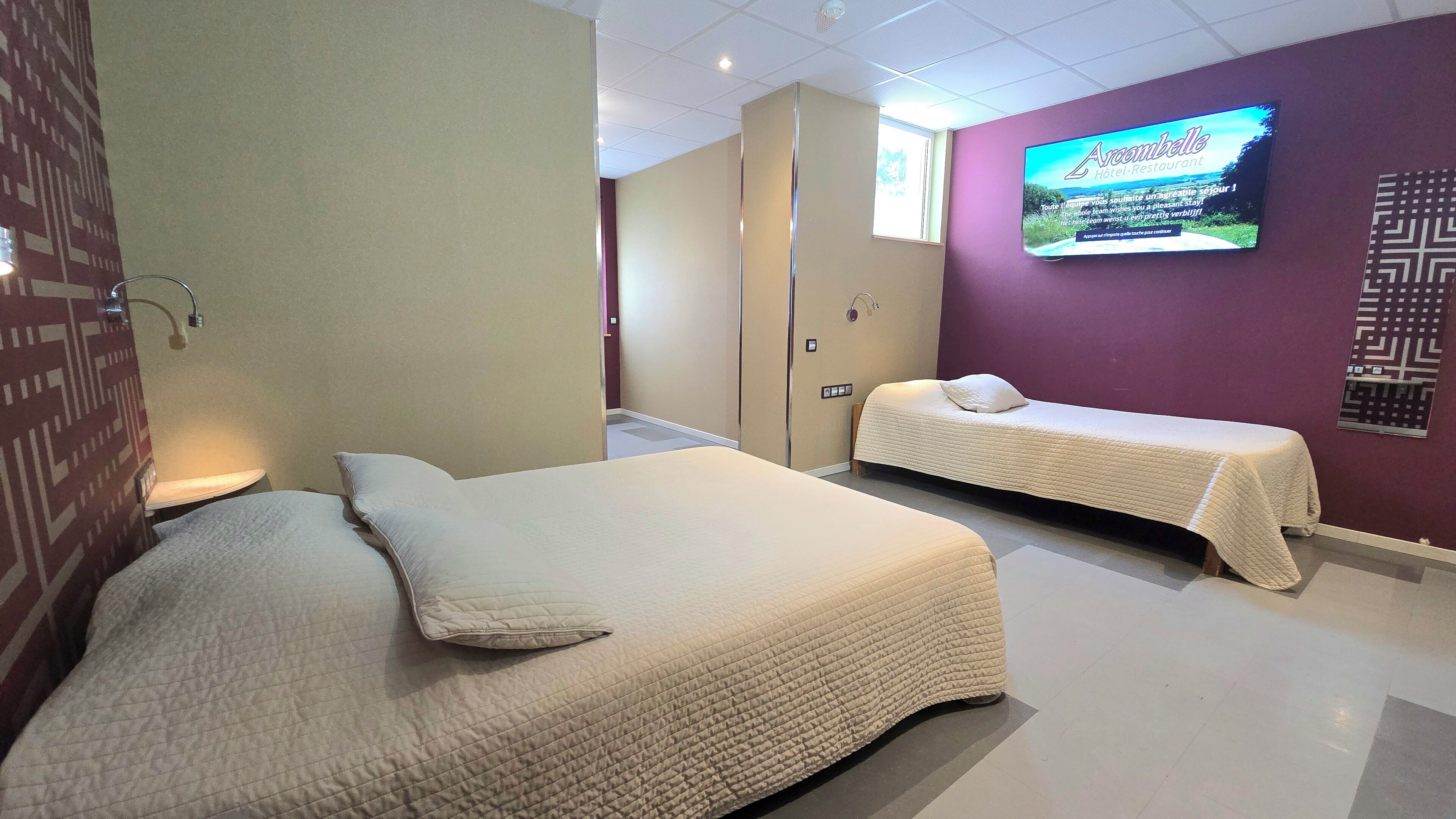 Et hotelværelse med to senge, et fjernsyn på væggen og et mønstret tapet.