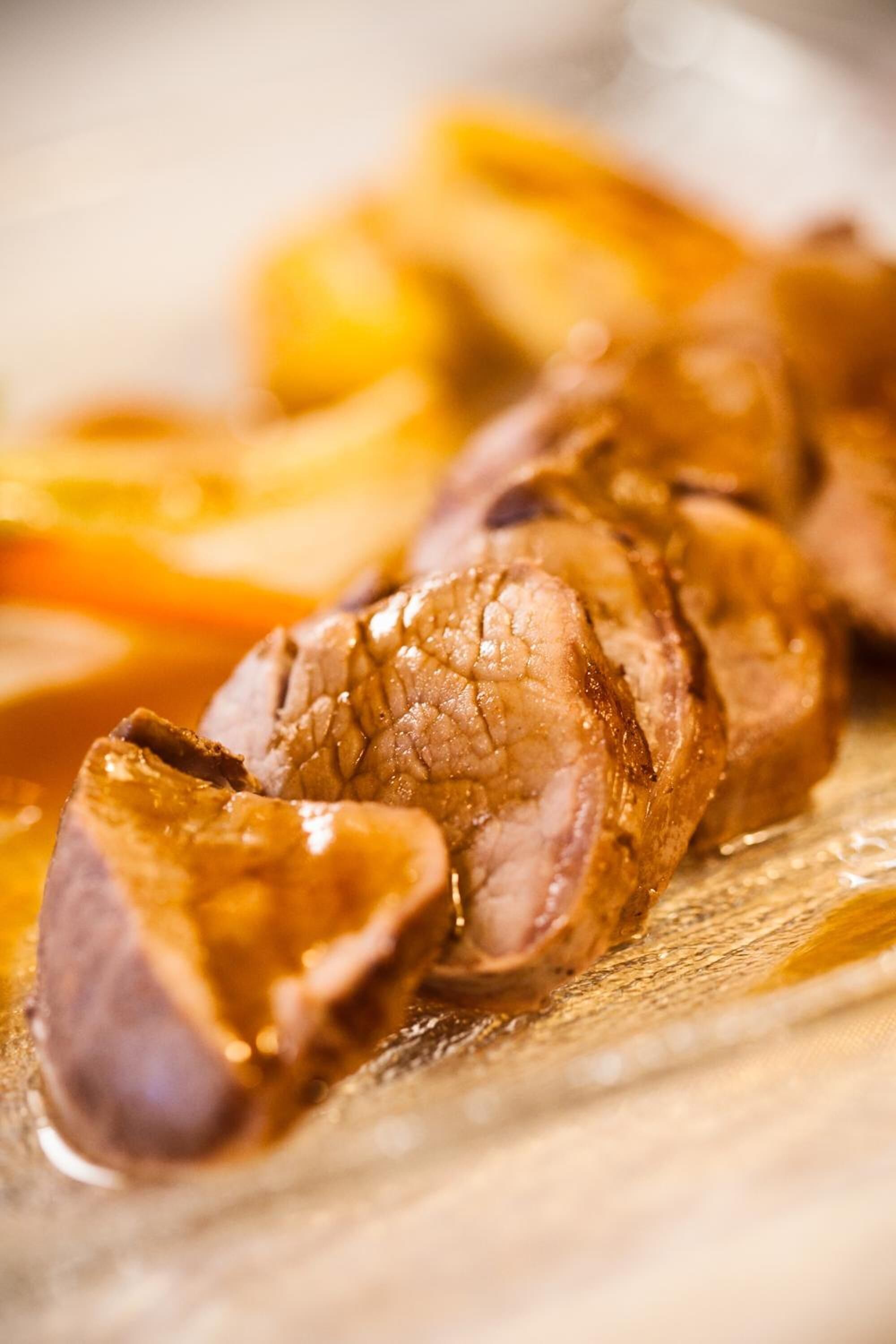 A close-up of sliced meat with a glossy sauce, likely beef, on a wooden surface.