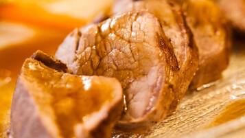 A close-up of sliced meat with a glossy sauce, likely beef, on a wooden surface.