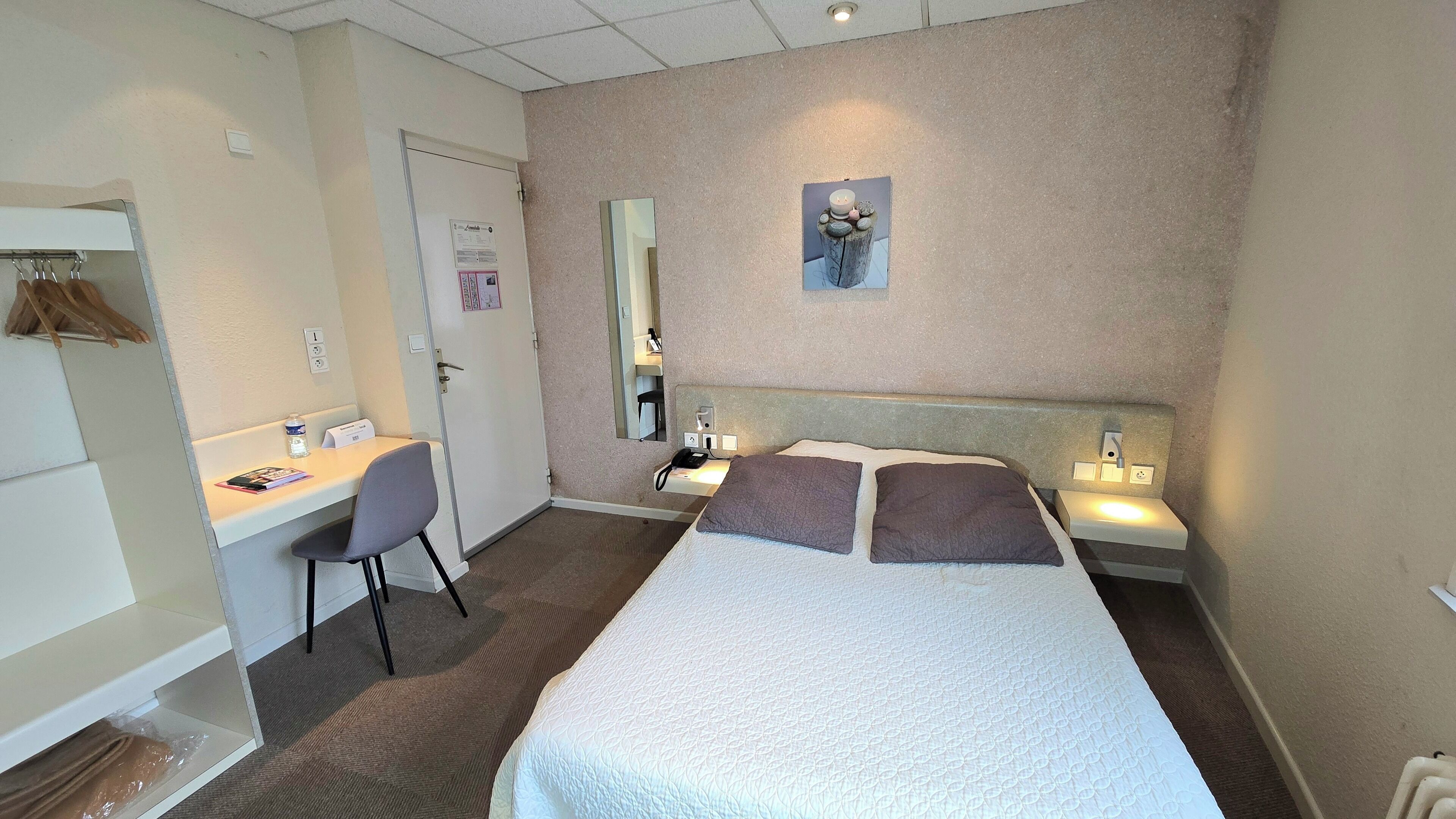 A hotel room with a bed, bedside table, chair, desk, and a mirror.