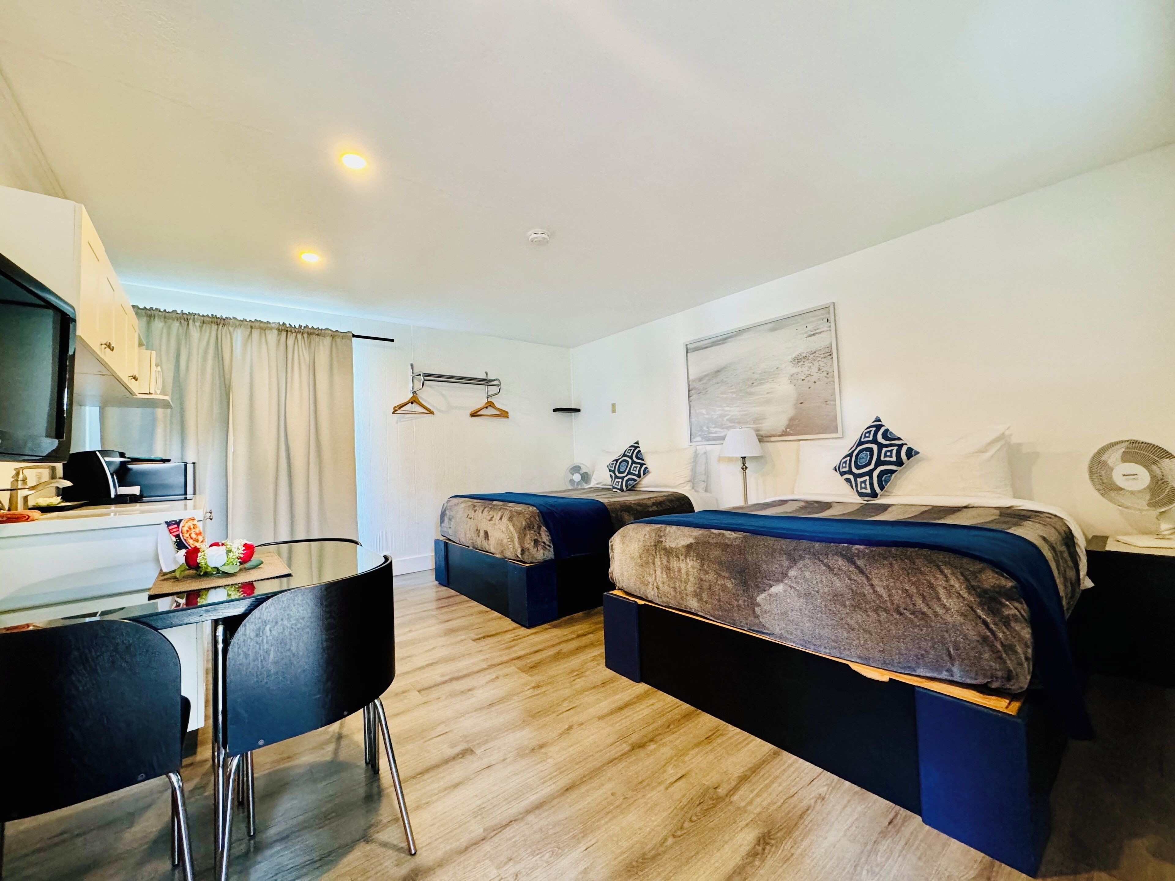 Habitación de hotel con escritorio, dos camas, una mesa de comedor, sillas, televisión y un cuadro en la pared.