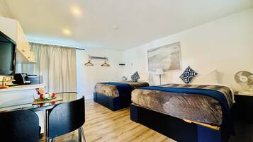 Habitación de hotel con escritorio, dos camas, una mesa de comedor, sillas, televisión y un cuadro en la pared.