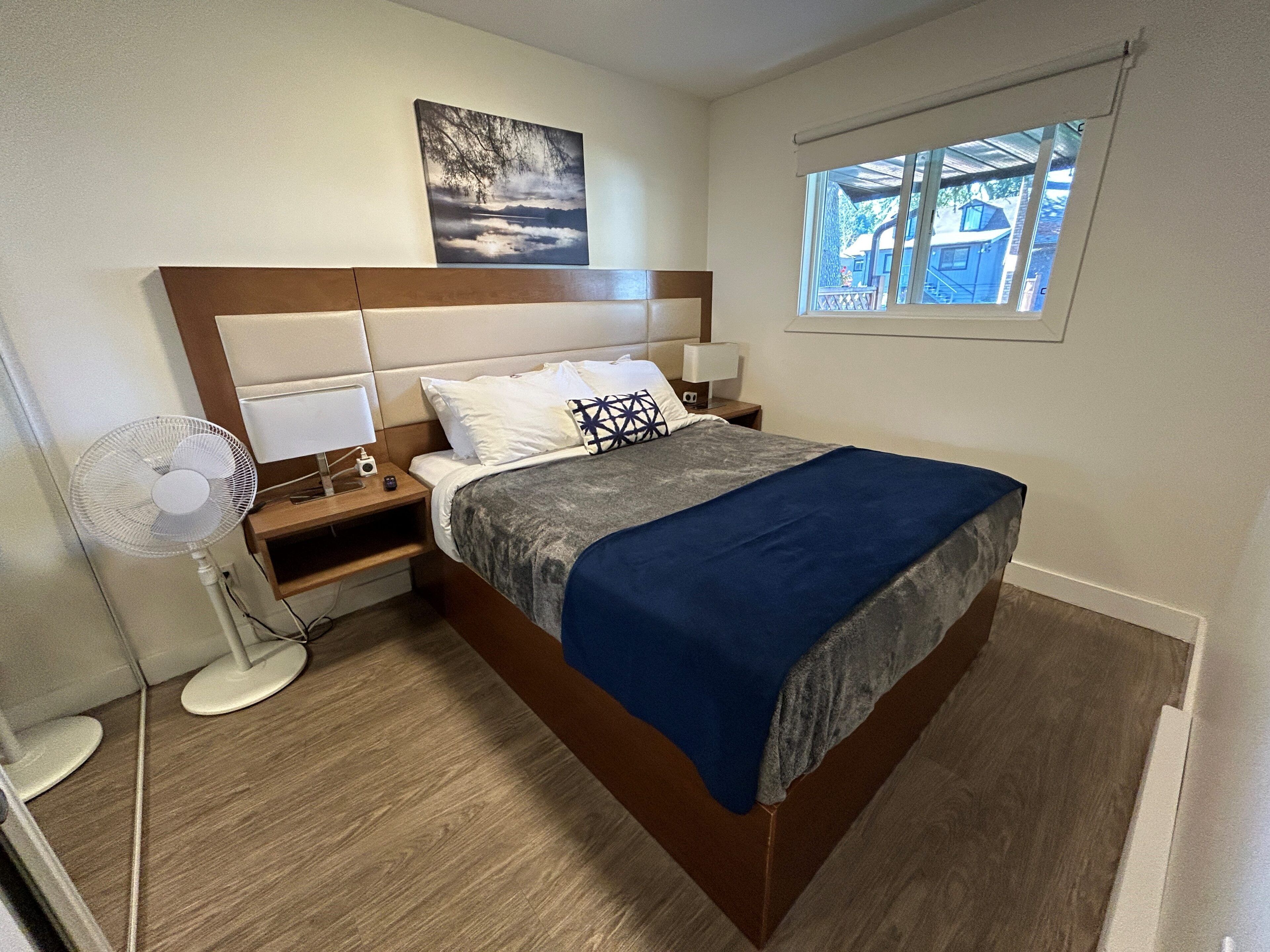 A bedroom with a bed, bedside tables, a nightstand, a wall-mounted picture, and a window.
