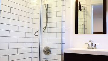 A modern bathroom with a glass-enclosed shower, white tiled walls, a white bathtub, and a black vanity with a mirror.