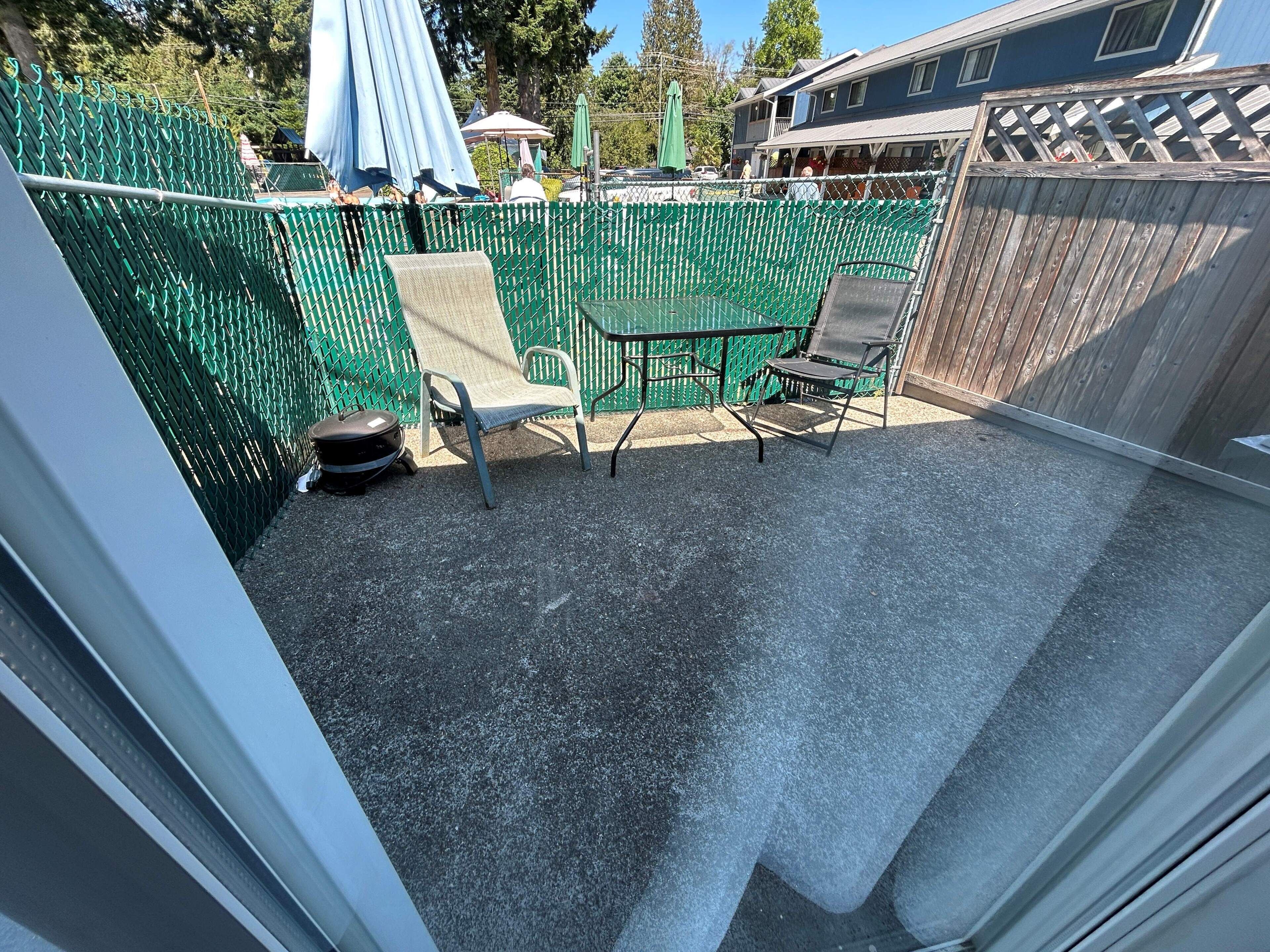 A patio with a green fence, two chairs, and a table.
