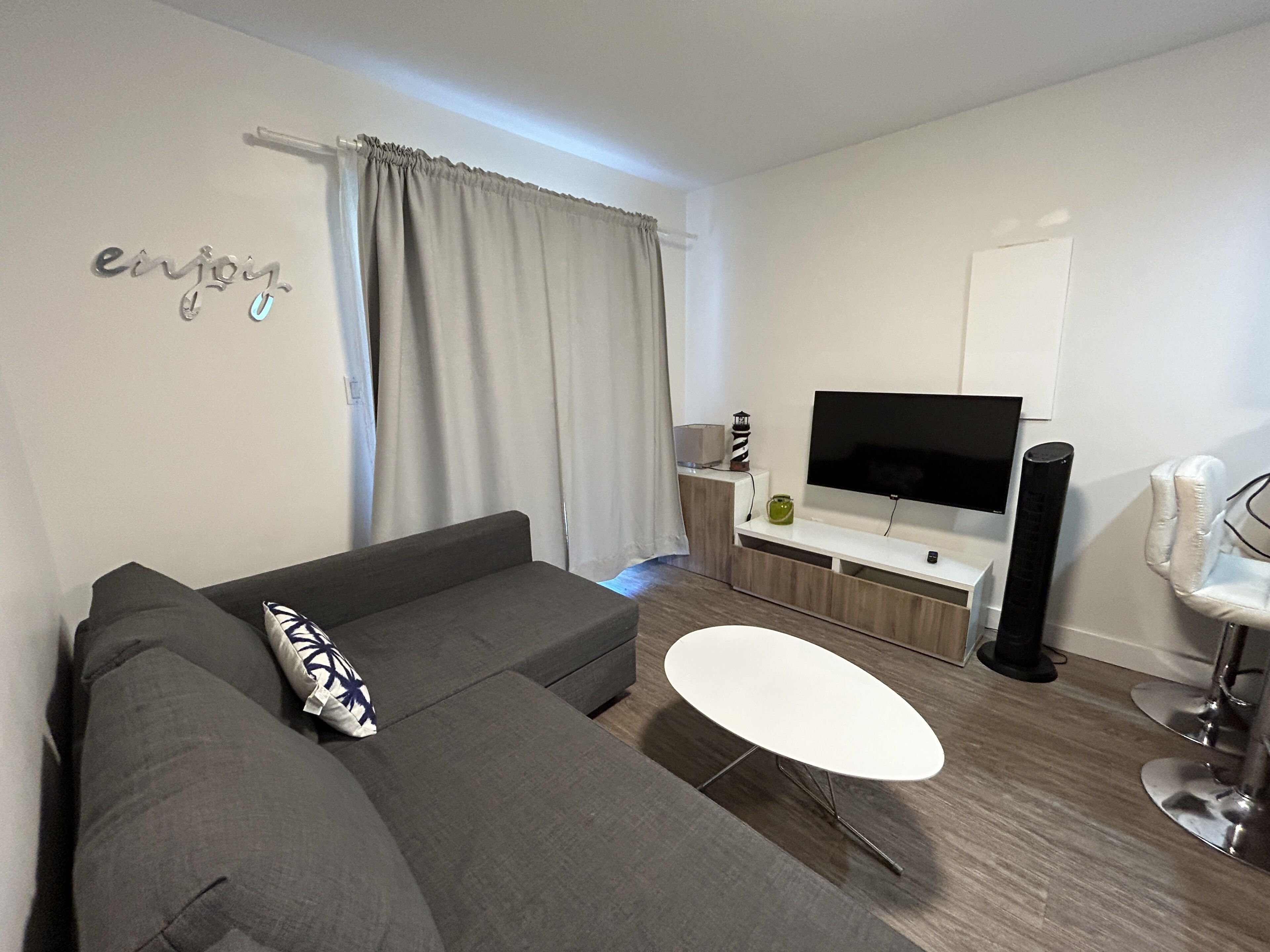 A modern living room with a grey sofa, a white coffee table, and a flat-screen TV on a wooden stand.