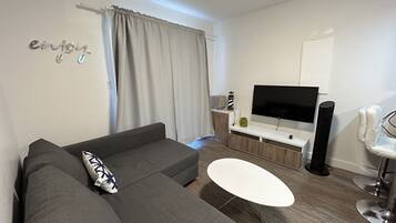 A modern living room with a grey sofa, a white coffee table, and a flat-screen TV on a wooden stand.