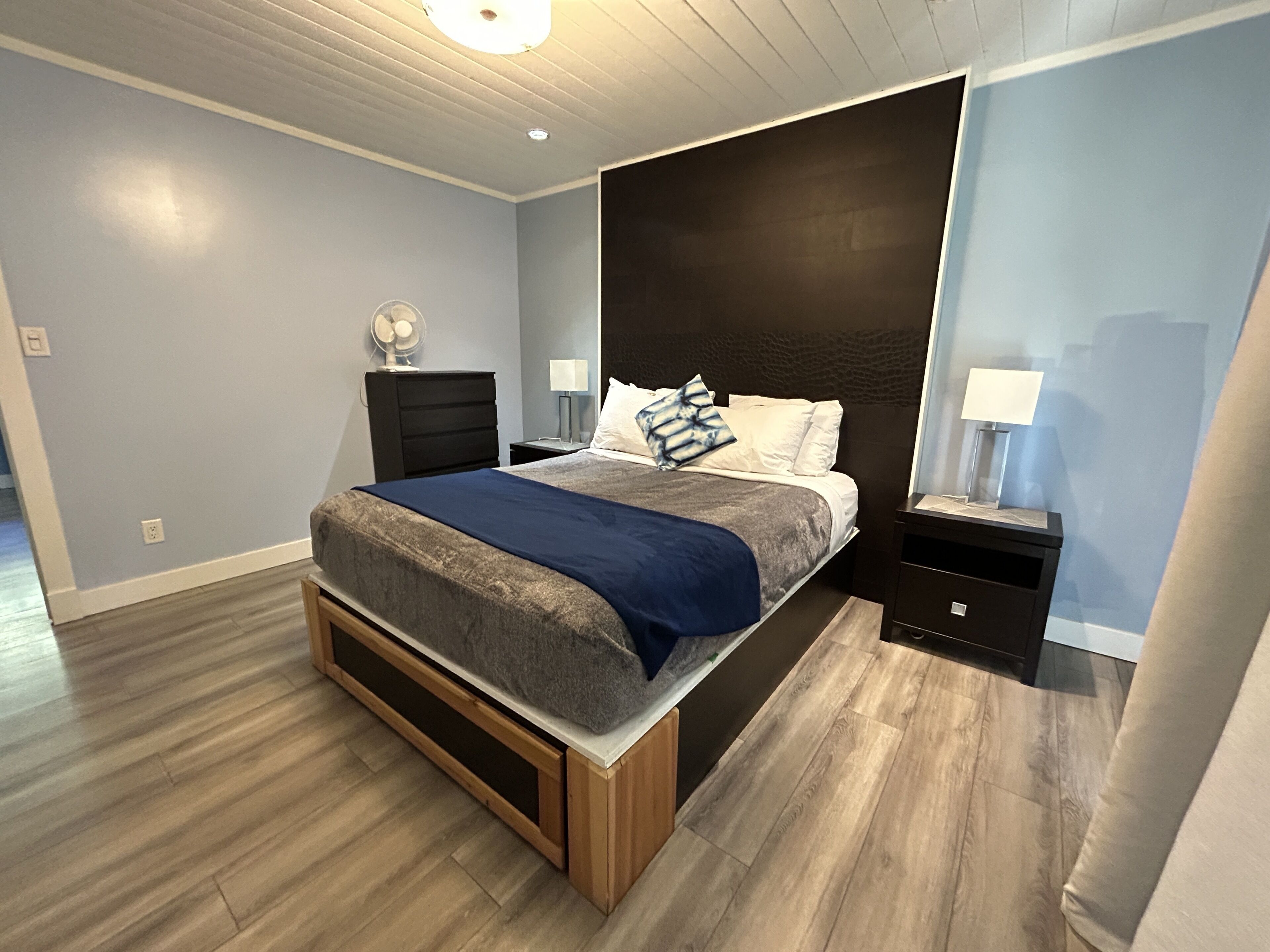A modern bedroom with a bed, nightstands, and a wooden floor.