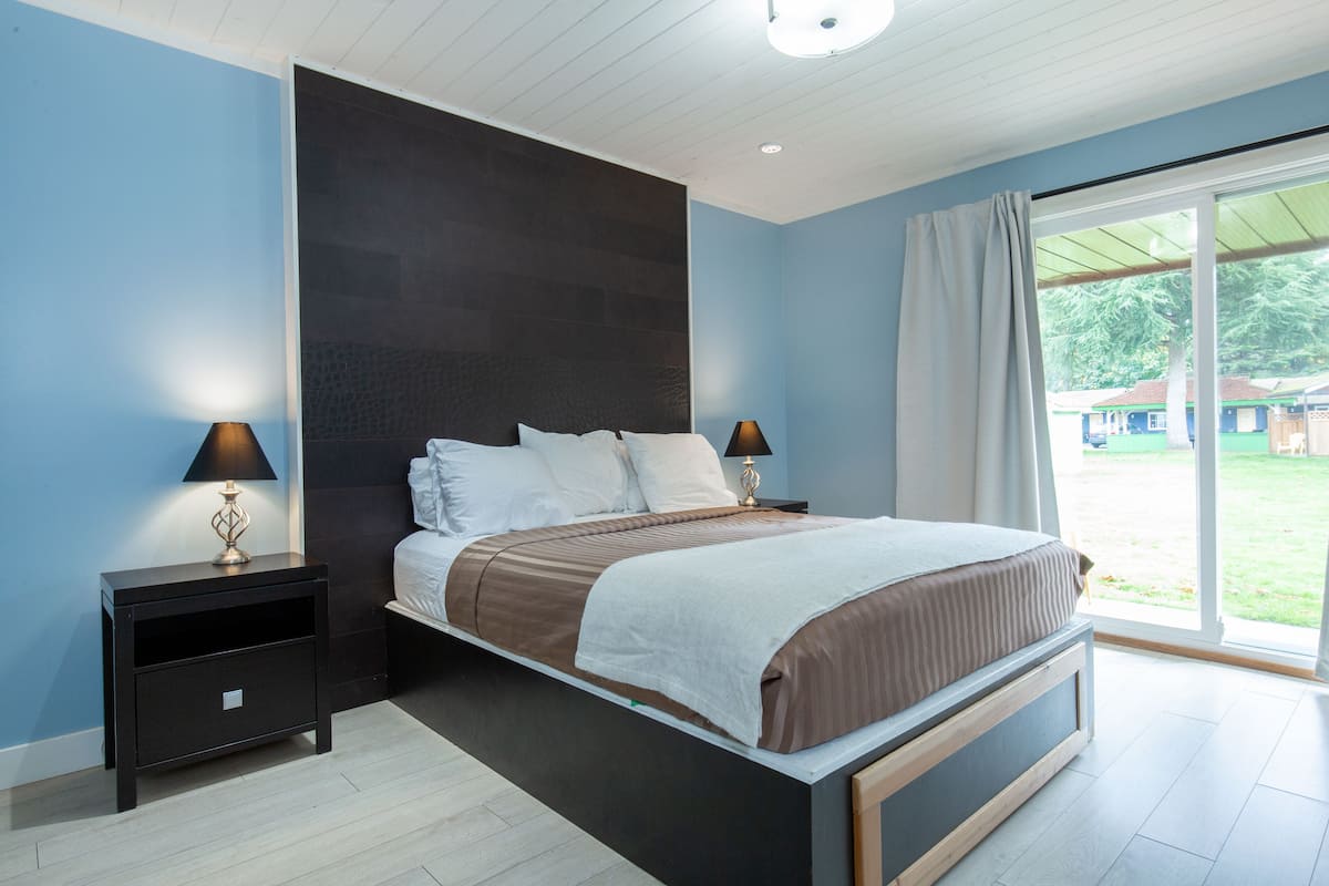 Ein modernes Schlafzimmer mit einem großen Bett, zwei Nachttischen mit Lampen und Blick ins Freie durch eine Schiebeglastür.