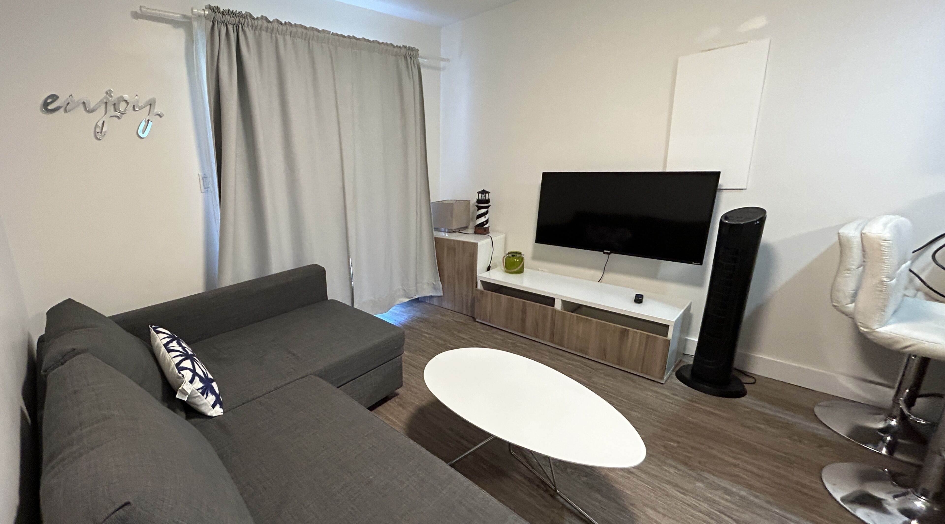 Ein modernes Wohnzimmer mit einem grauen Sofa, einem weißen Couchtisch und einem Flachbildfernseher auf einem Holzboden.