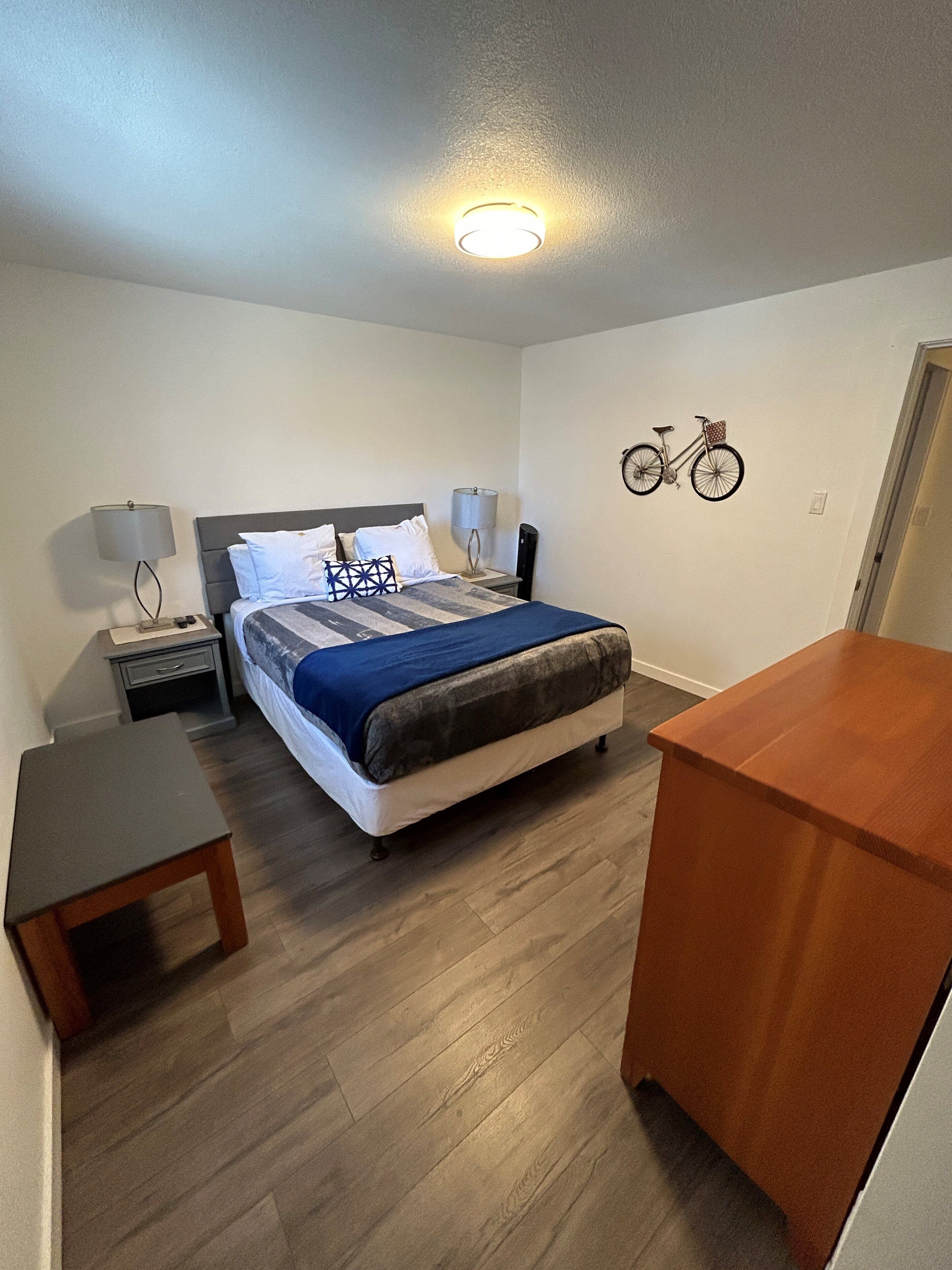 Een slaapkamer met een bed, nachtkastjes, een bureau en een aan de muur bevestigde fiets.