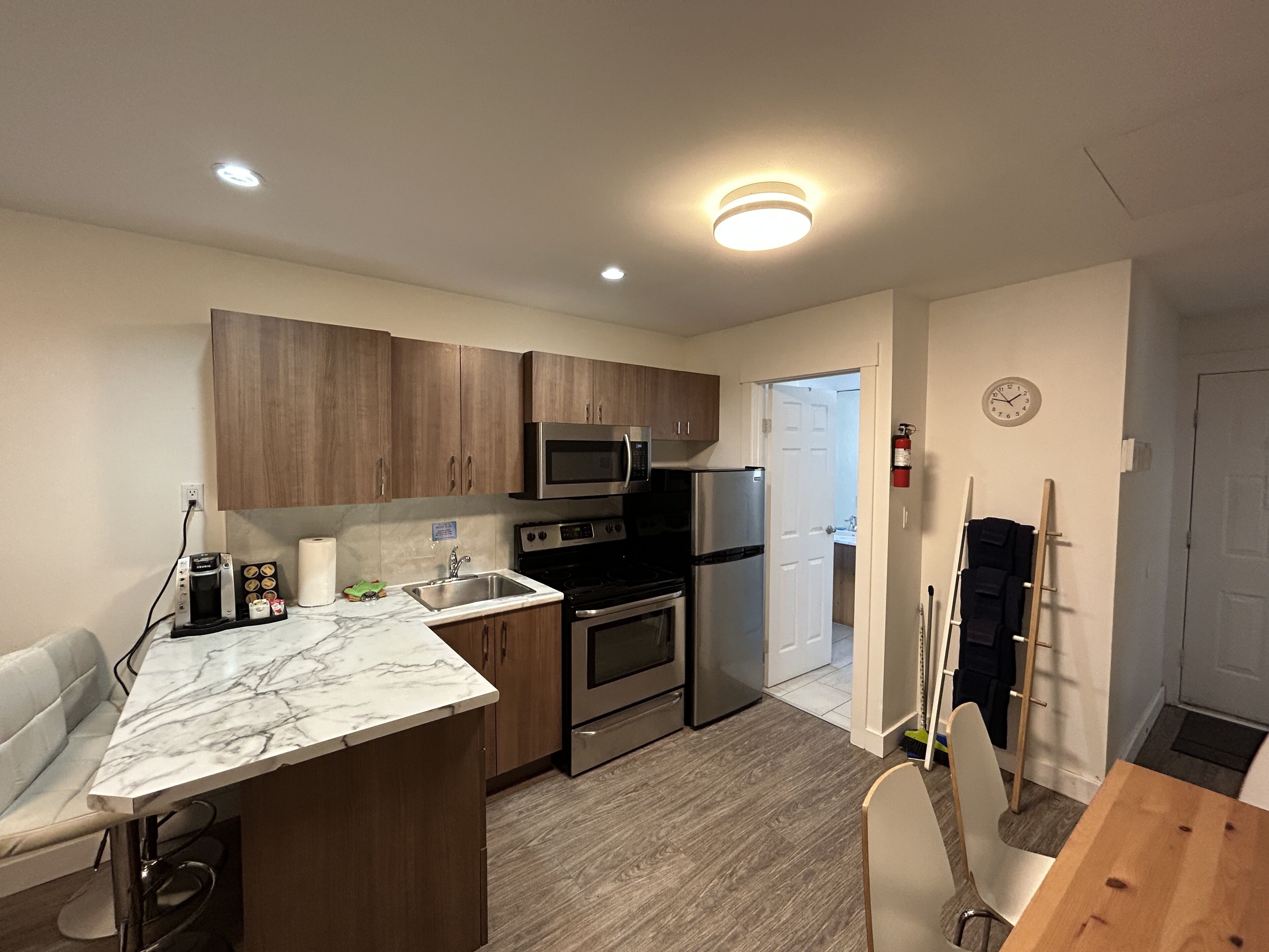 A modern kitchen with wooden cabinets, stainless steel appliances, a marble countertop, and a dining area with a wooden table and chairs.