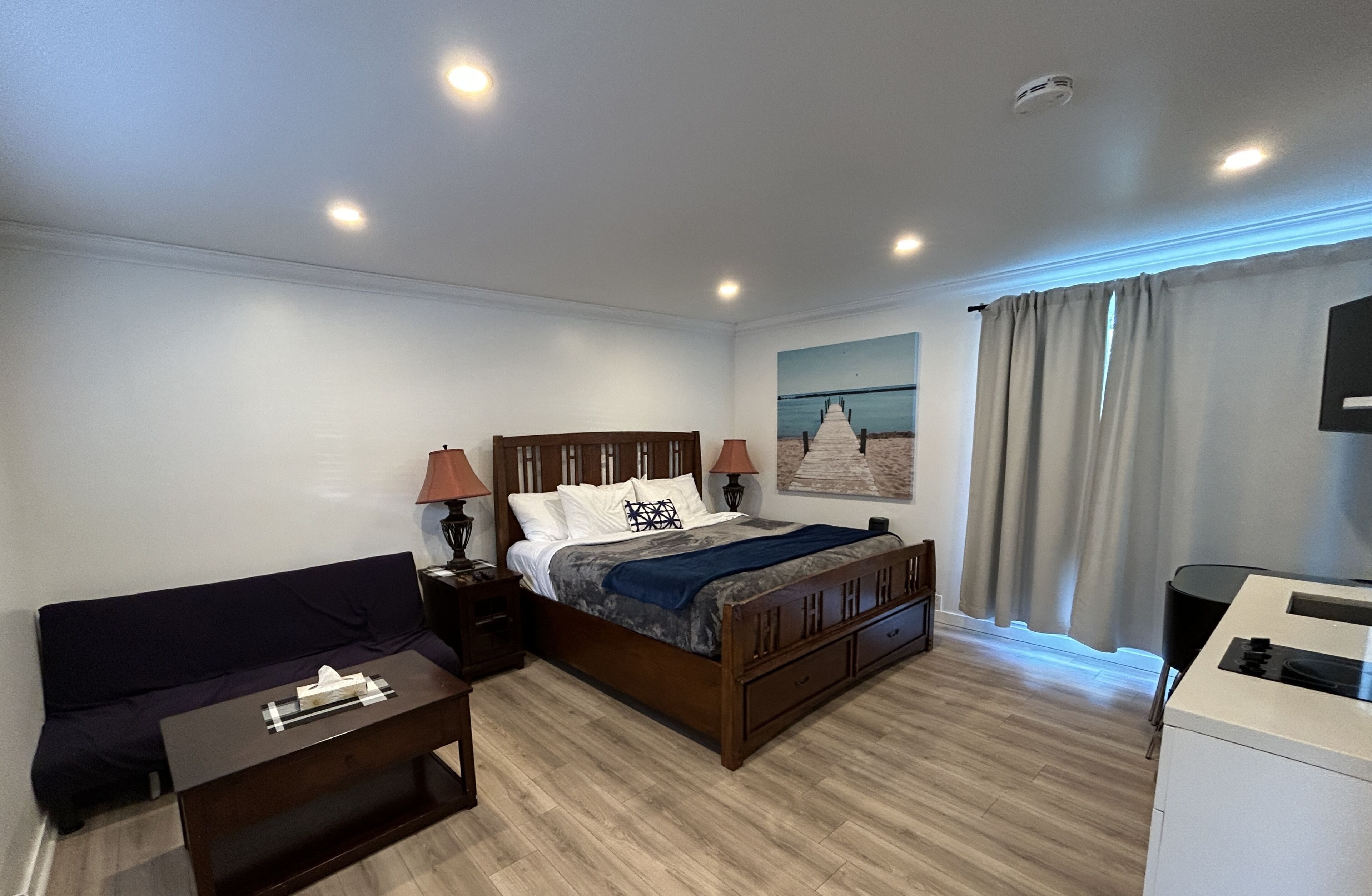 A hotel room with a bed, a desk, a chair, a TV, and a painting on the wall.