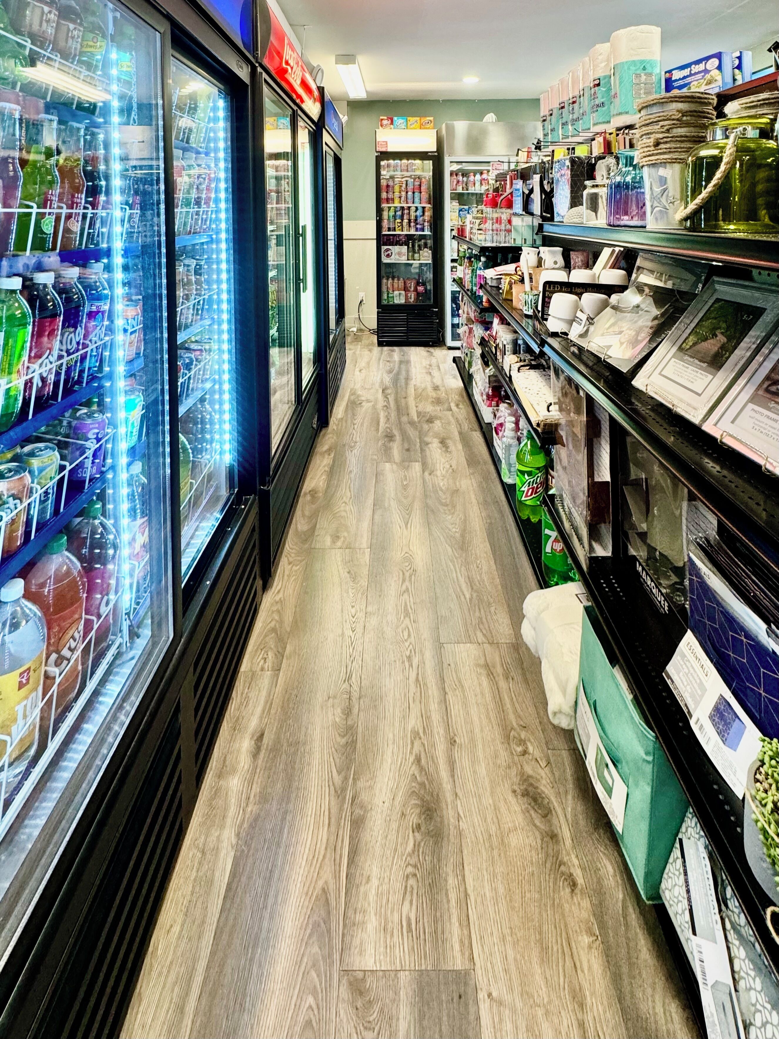 A store aisle with refrigerated beverage dispensers on the left and shelves stocked with various products on the right.