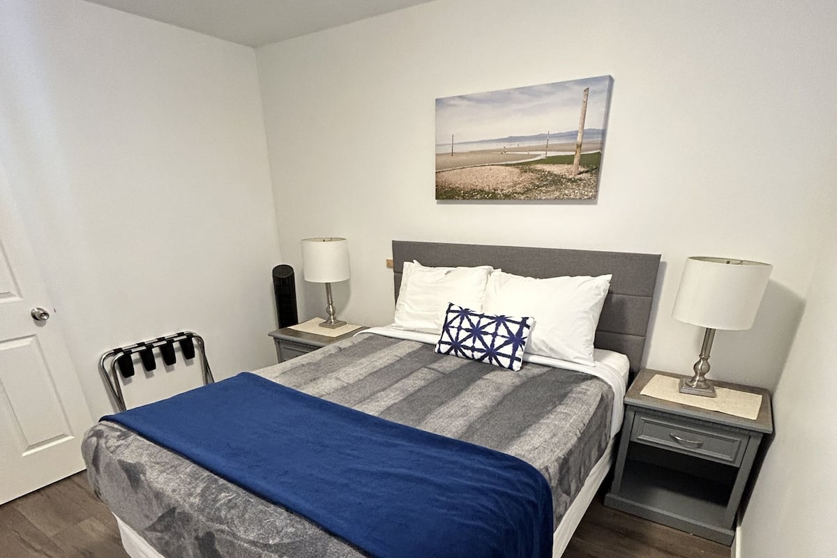 Ein ordentlich eingerichtetes Hotelzimmer mit einem großen Bett, zwei Nachttischen, einer Kopfteil und einem Bild an der Wand sowie einer Tür.