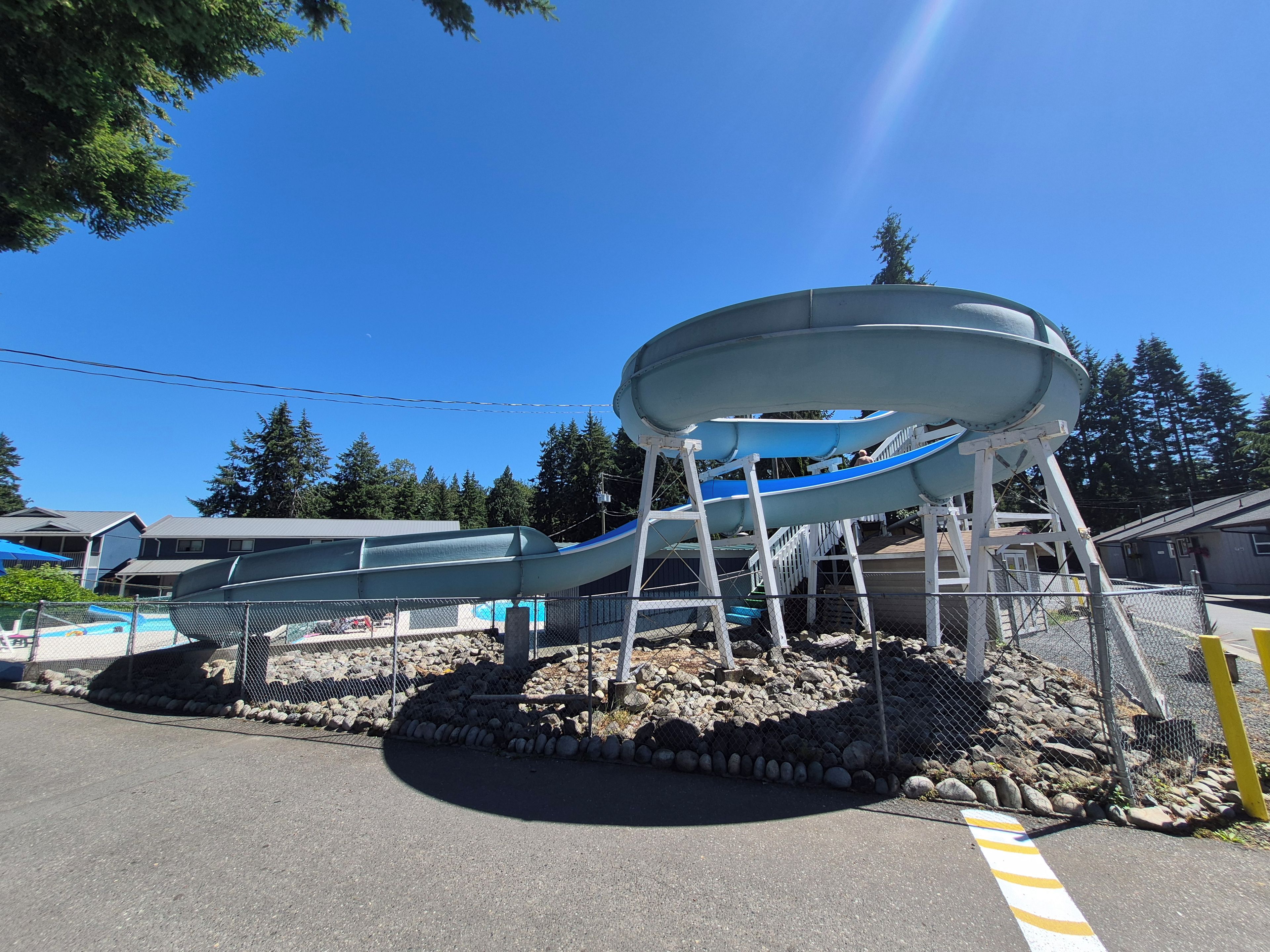 A water slide structure with a circular design, surrounded by a fence and a pile of rocks.