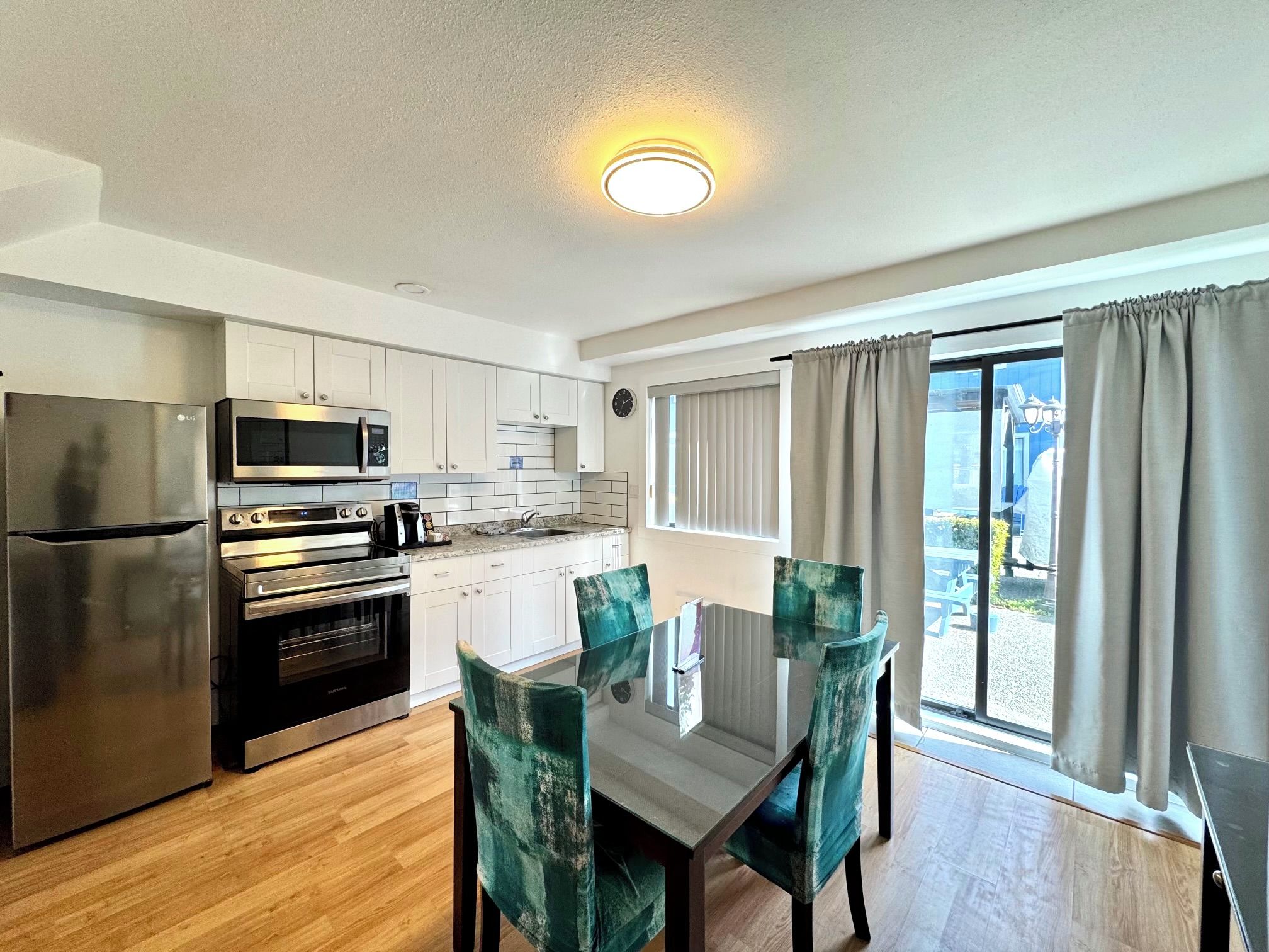 A modern kitchen with stainless steel appliances, a dining area with a glass table, and a view through large windows.