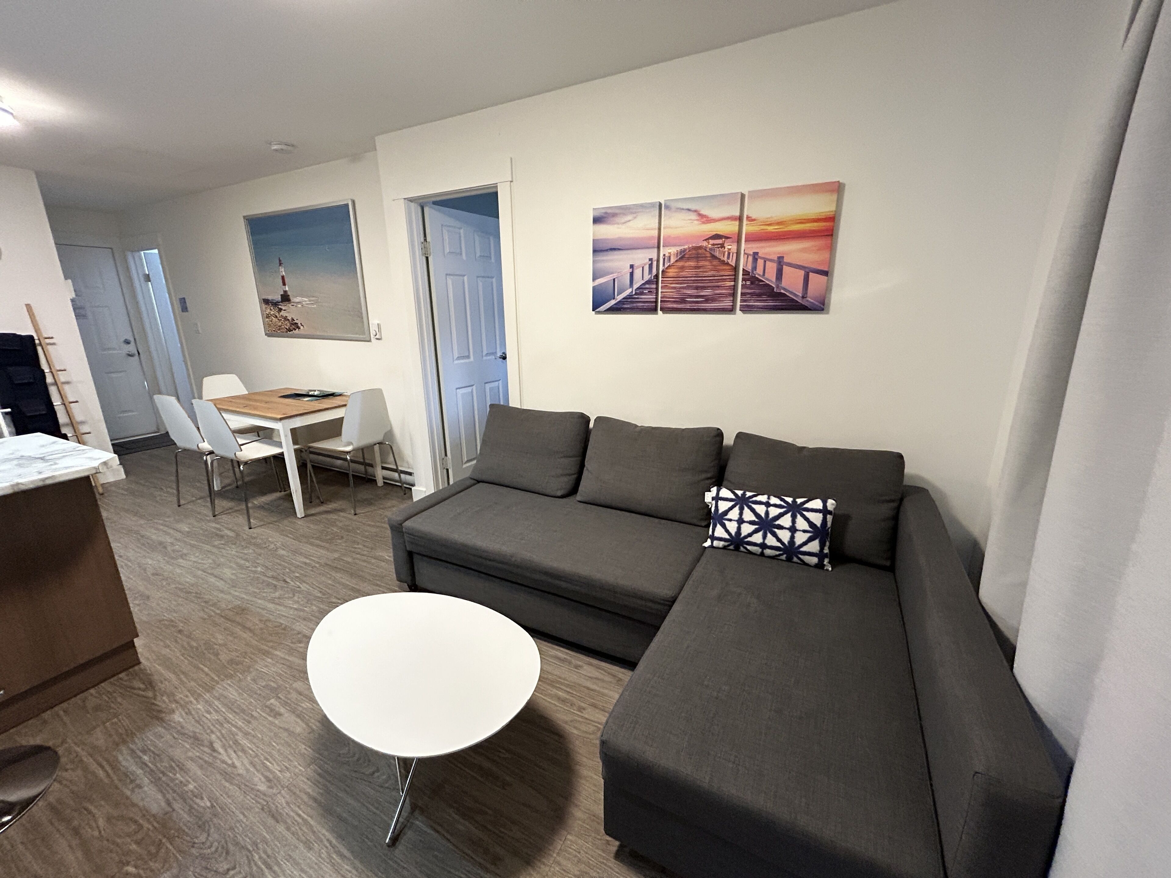 A modern living room with a grey sofa, a white coffee table, and a dining area with a wooden table and white chairs.