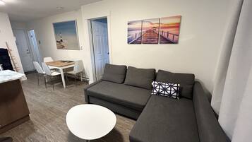 A modern living room with a grey sofa, a white coffee table, and a dining area with a wooden table and white chairs.